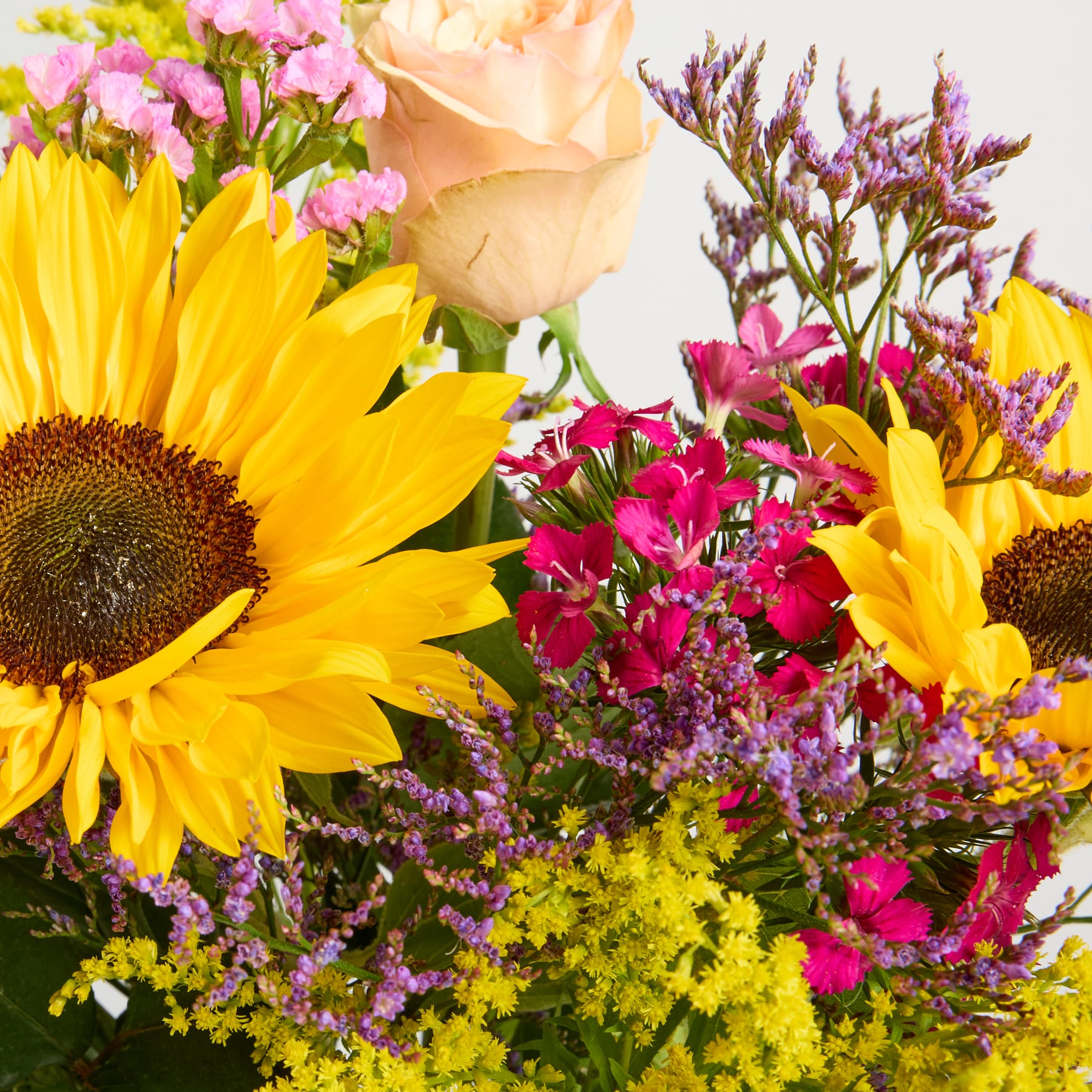 Ein lebendiger Strauß aus Sonnenblumen, Rosen und anderen bunten Blumen vor einem unscharfen natürlichen Hintergrund.