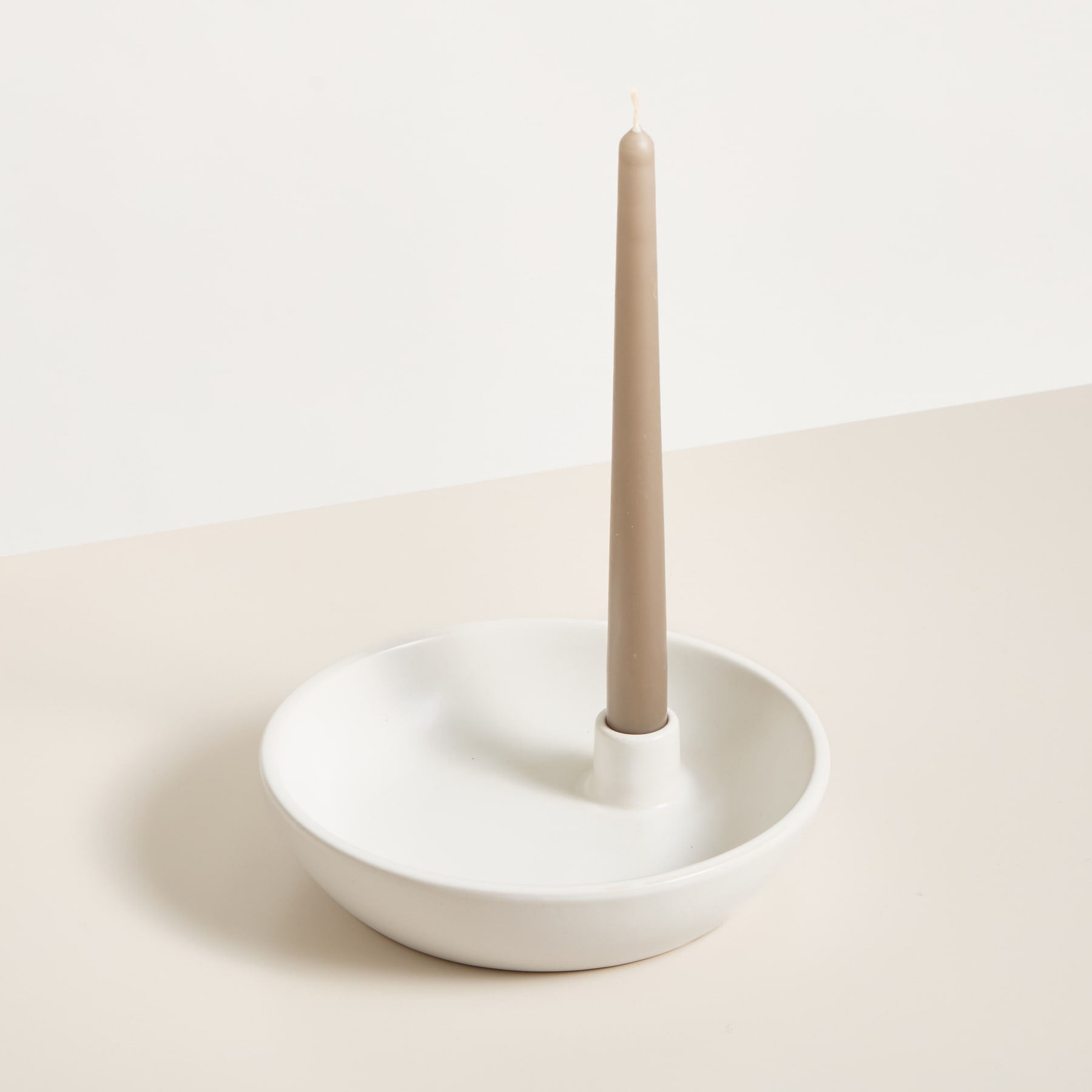 Eine einfache, minimalistische weiße Keramikschale mit einem kleinen zylindrischen Vorsprung in der Mitte, die auf einer schlichten, hellen Oberfläche ruht.
