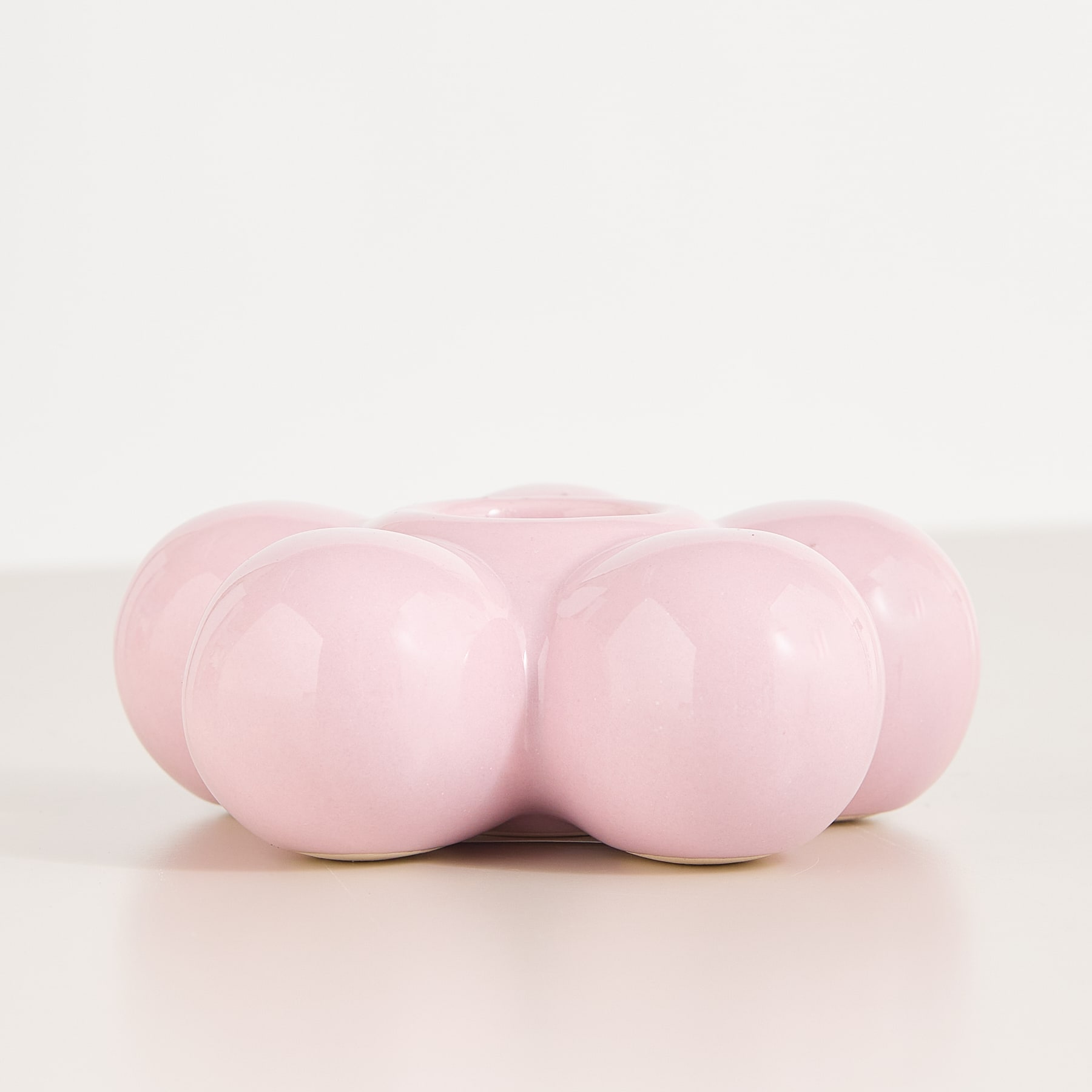 Ein rosafarbener, ballonartiger Sockel trägt eine Holzsäule in einer minimalistischen, beigefarbenen Umgebung.