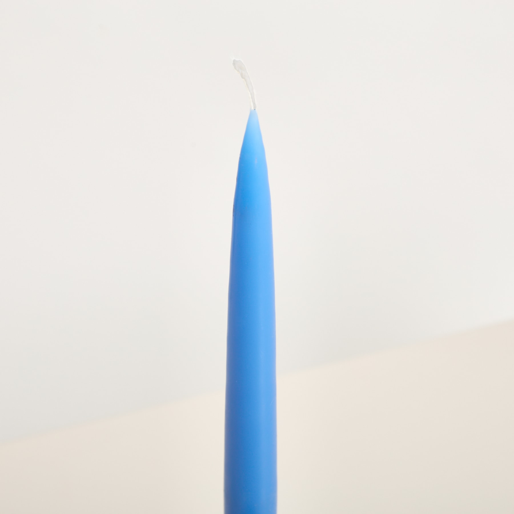 Ein einzelner blauer Buntstift steht aufrecht vor einem schlichten, hellen Hintergrund.