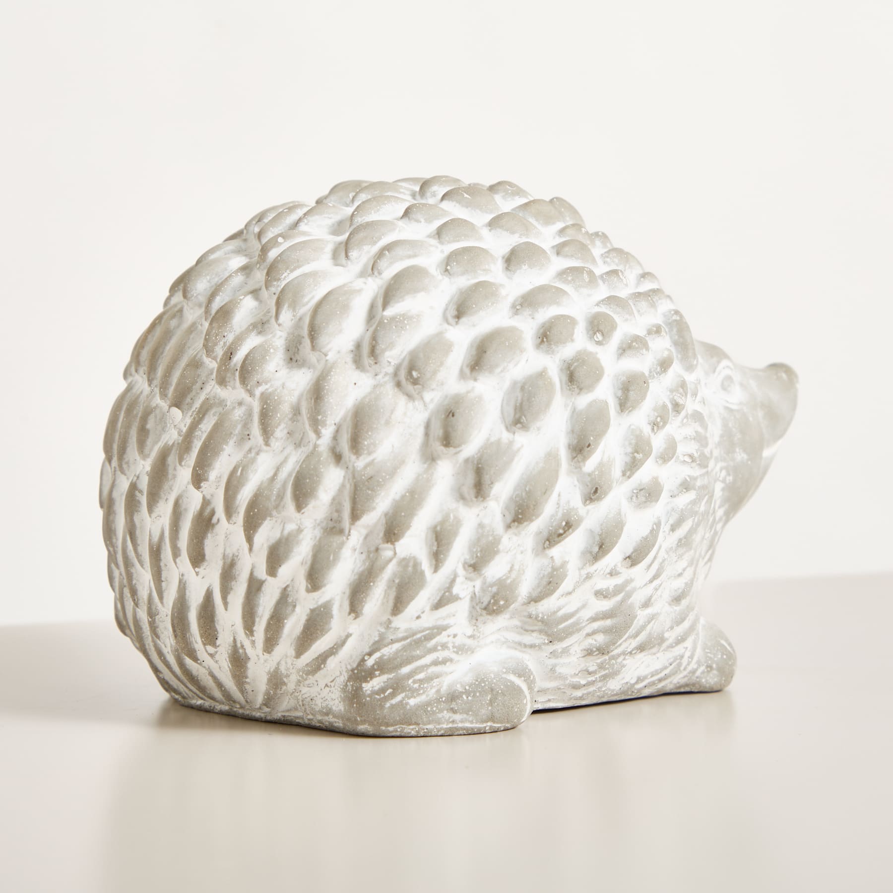 Eine weiße, strukturierte Keramikskulptur, die einem Igel oder Stachelschwein ähnelt, sitzt auf einer schlichten, hellen Oberfläche.
