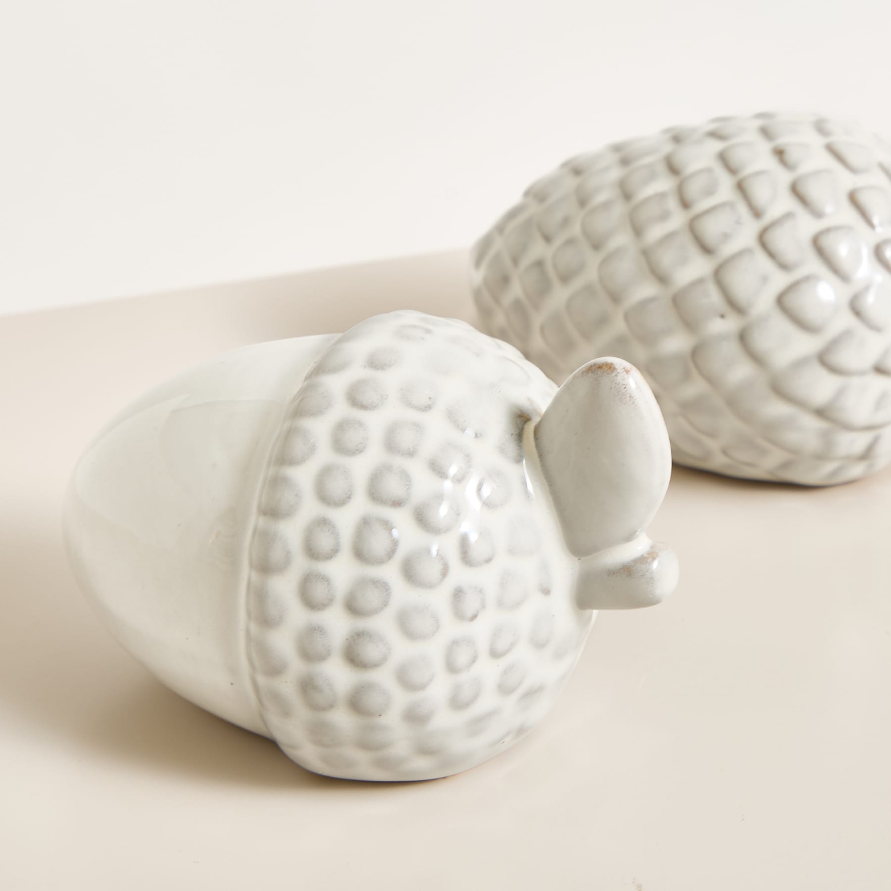 Das Bild zeigt zwei weiße Keramikobjekte mit einer strukturierten, gemusterten Oberfläche, die an einen Golfball erinnert. Sie sind auf einer hellen Oberfläche platziert, wodurch eine minimalistische und klare visuelle Komposition entsteht.