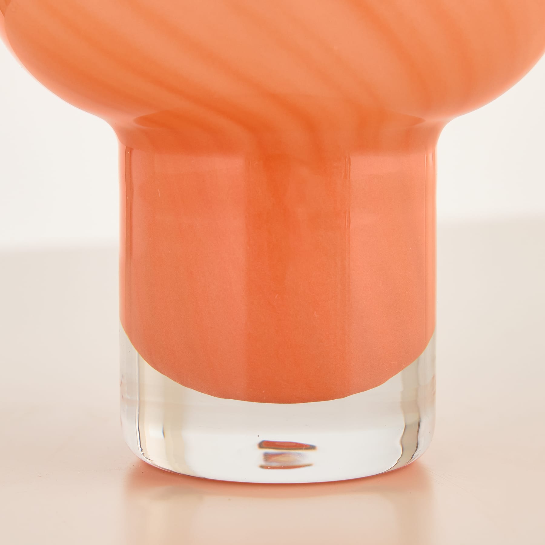 Ein leuchtend orangefarbener Glasbehälter mit durchsichtigem Boden steht auf einer hellen Oberfläche.