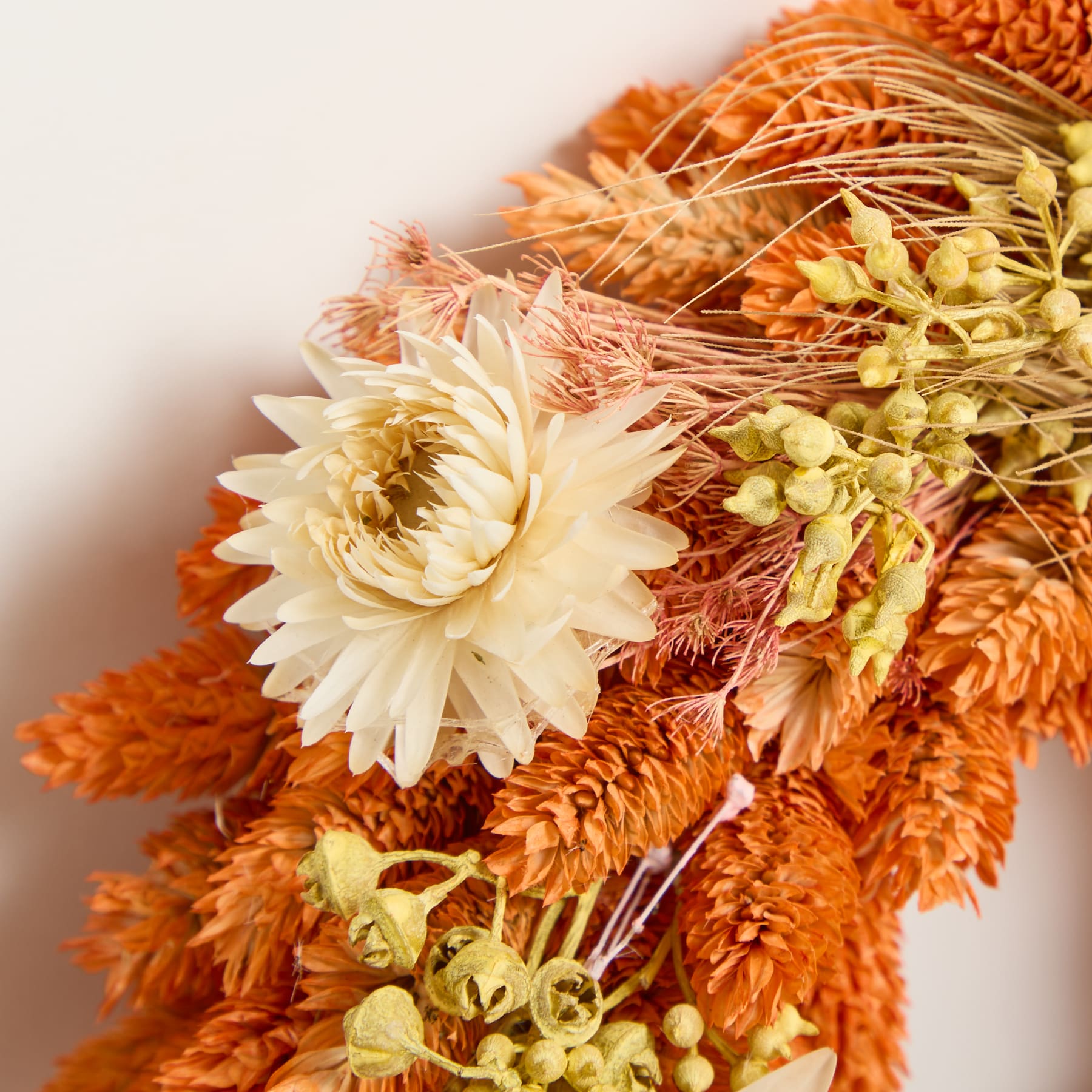 Ein lebendiger Strauß orangefarbener und gelber Trockenblumen, darunter Chrysanthemen und andere strukturierte florale Elemente, vor einem schlichten Hintergrund.