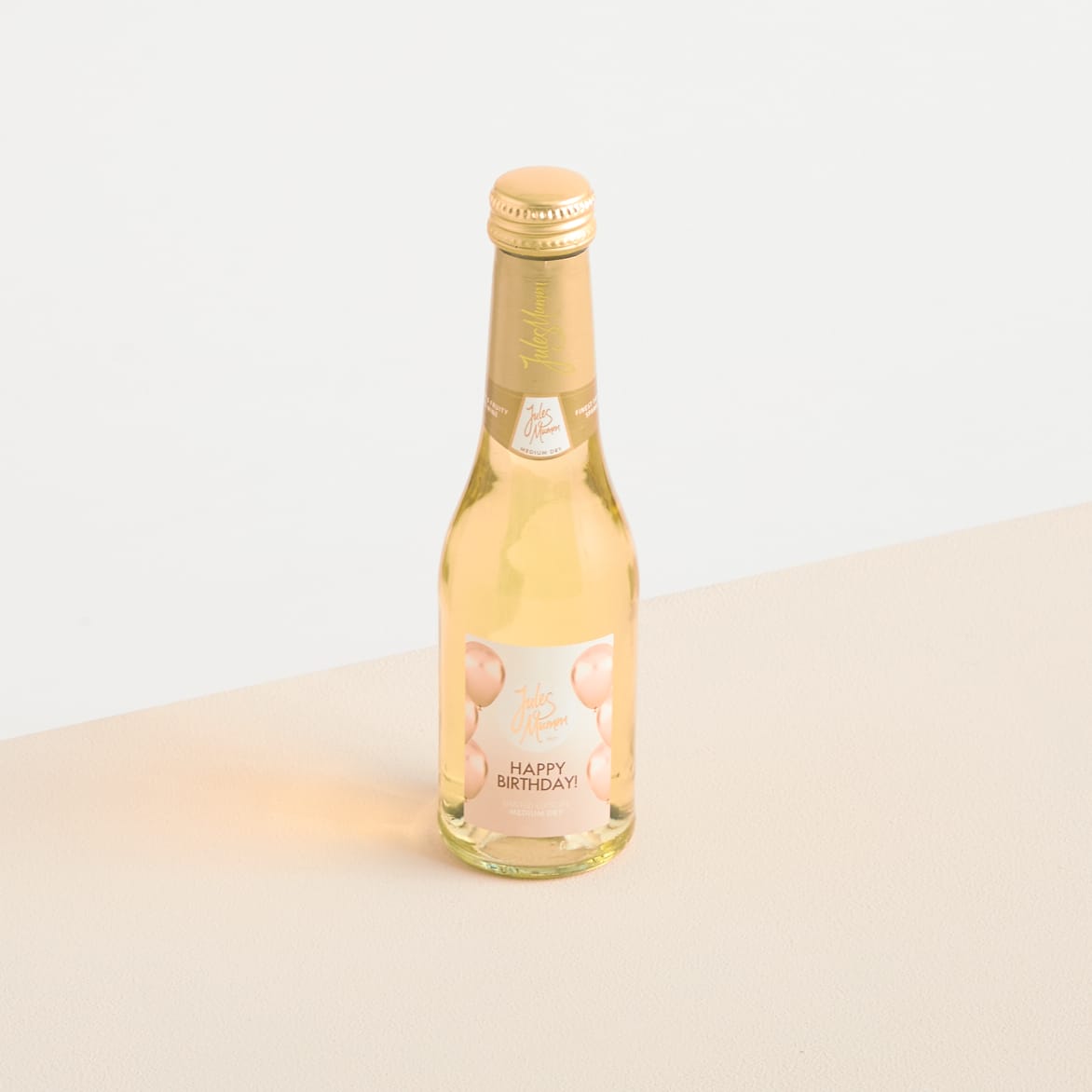 Eine Glasflasche Sekt oder Champagner mit dem Etikett „Happy Birthday“ auf hellem Hintergrund.