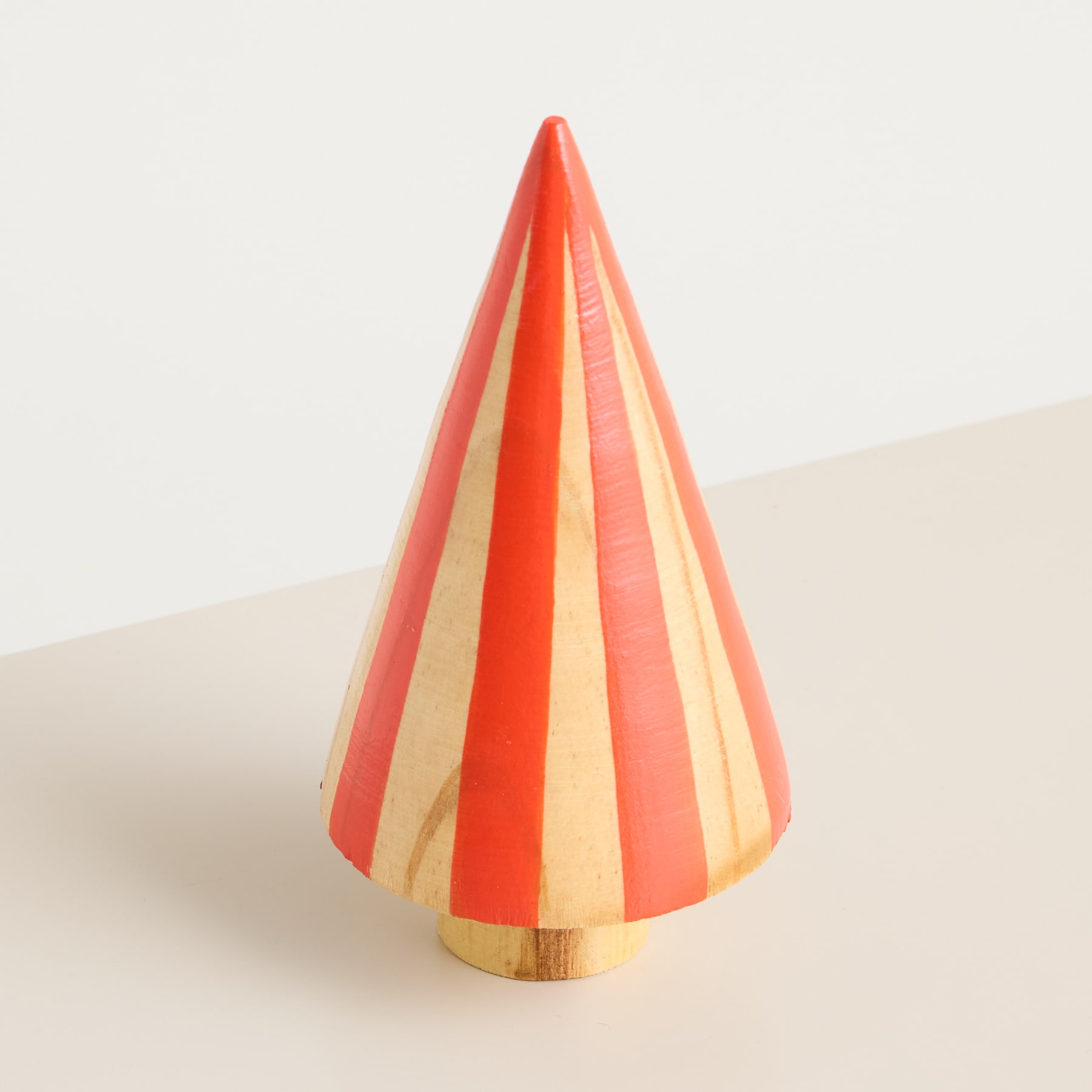 Auf einer schlichten, hellen Oberfläche steht ein leuchtend gestreiftes, kegelförmiges Objekt.