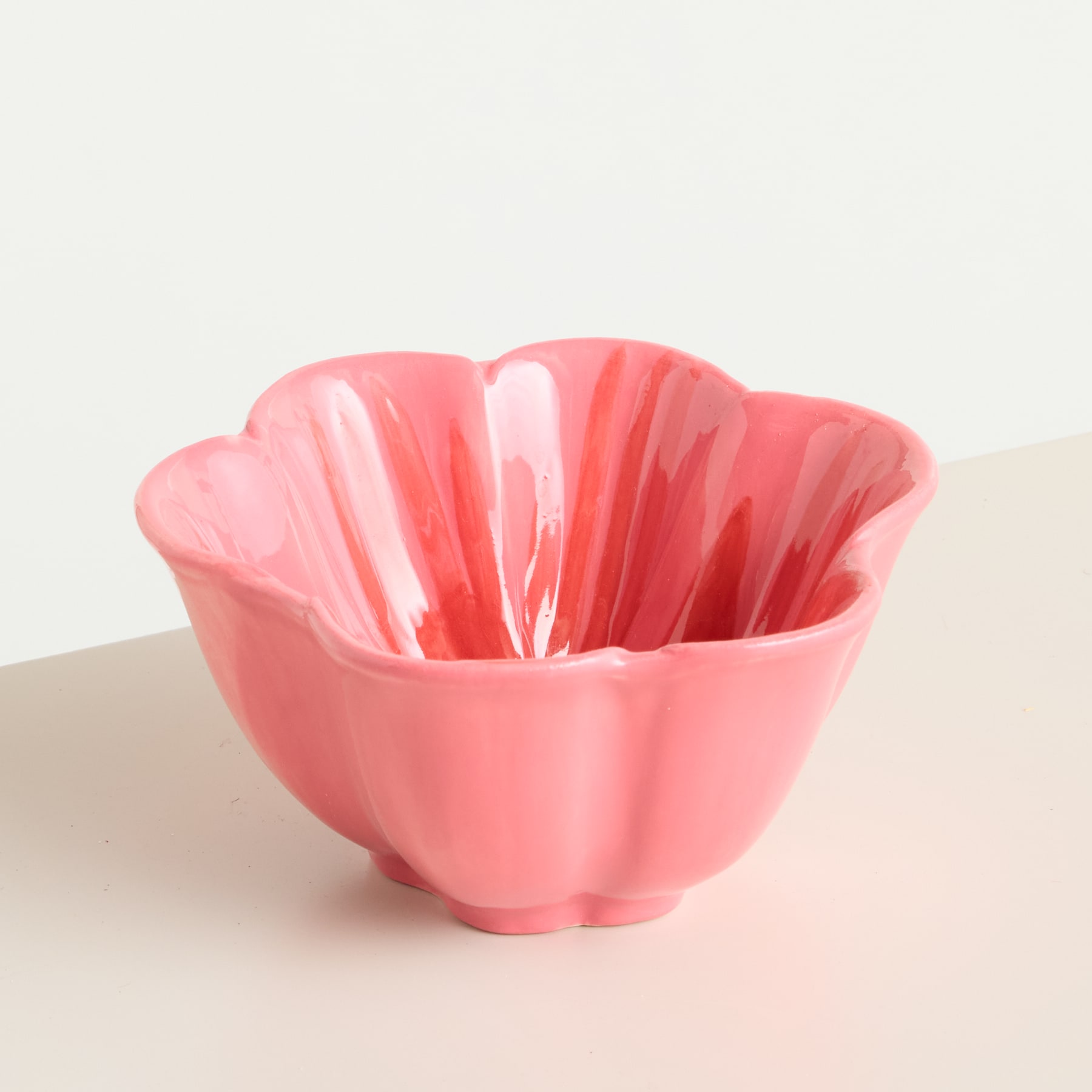 Eine leuchtend rosa, geriffelte Keramikschale steht auf einer Oberfläche in neutraler Farbe und schafft so eine optisch beeindruckende und minimalistische Komposition.