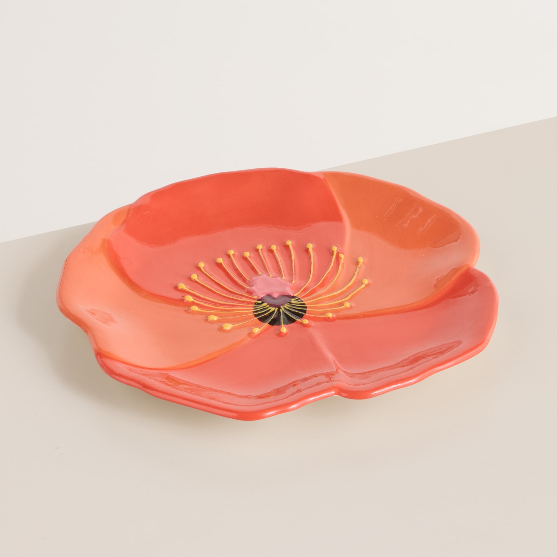 Auf einer hellen Oberfläche steht eine leuchtend orangefarbene Keramikschale in Blumenform.