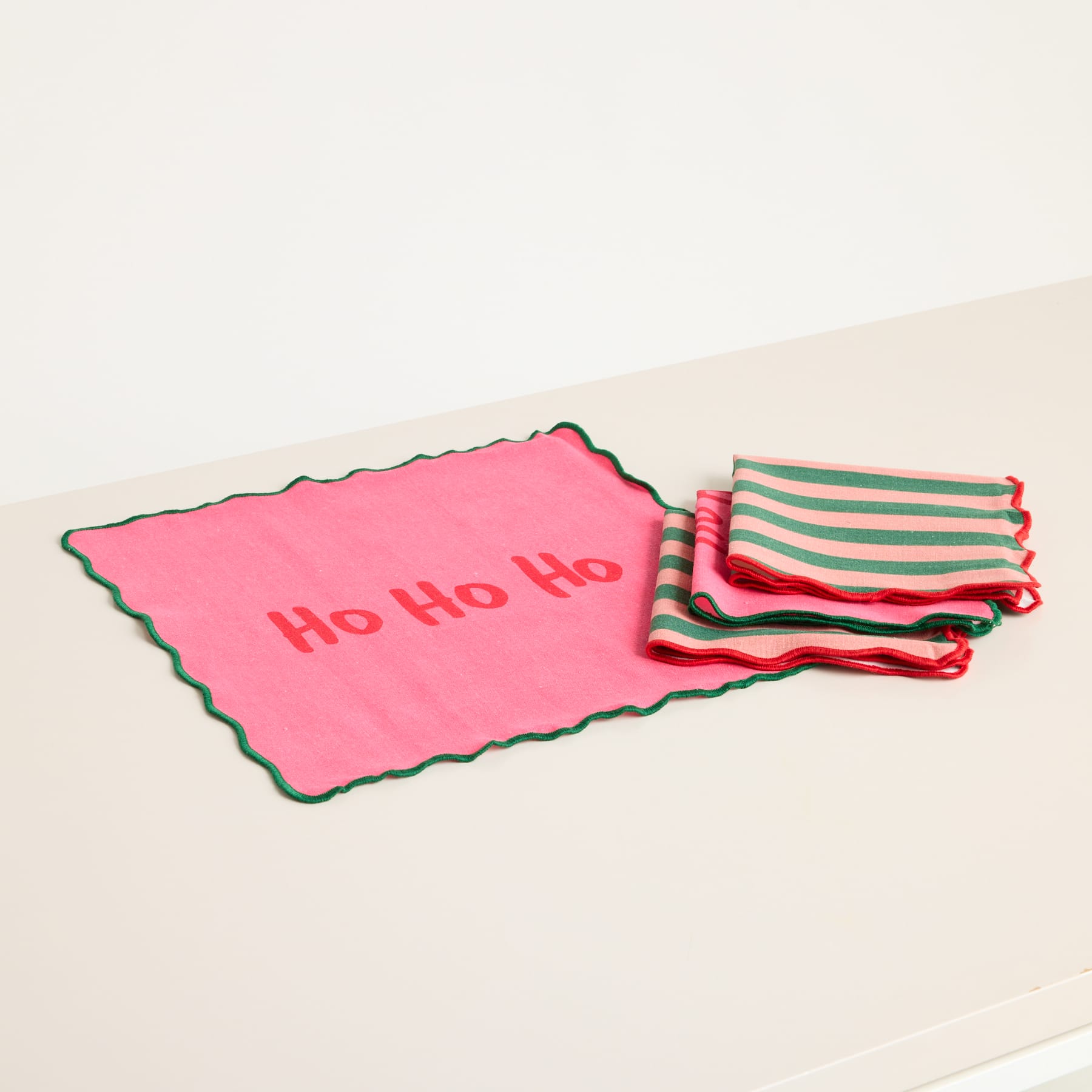 Das Bild zeigt eine rosa Karte mit dem Text „Ho Ho Ho“ und mehrere rot und grün gestreifte Karten oder Zettel daneben, alles auf einem schlichten weißen Hintergrund.