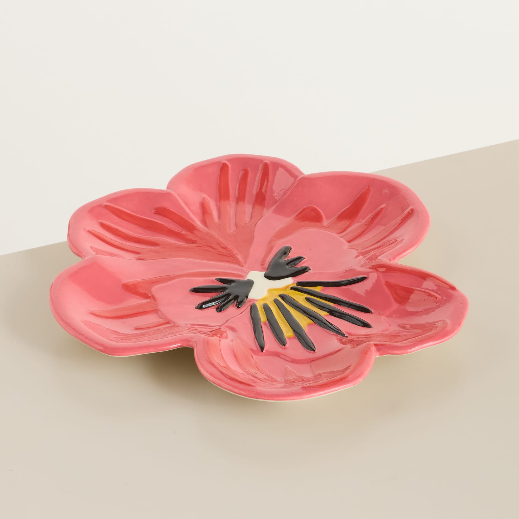 Auf einer hellen Oberfläche steht eine leuchtend rosa Keramikschale in Blumenform, deren Blütenblätter und Details in der Mitte deutlich sichtbar sind.