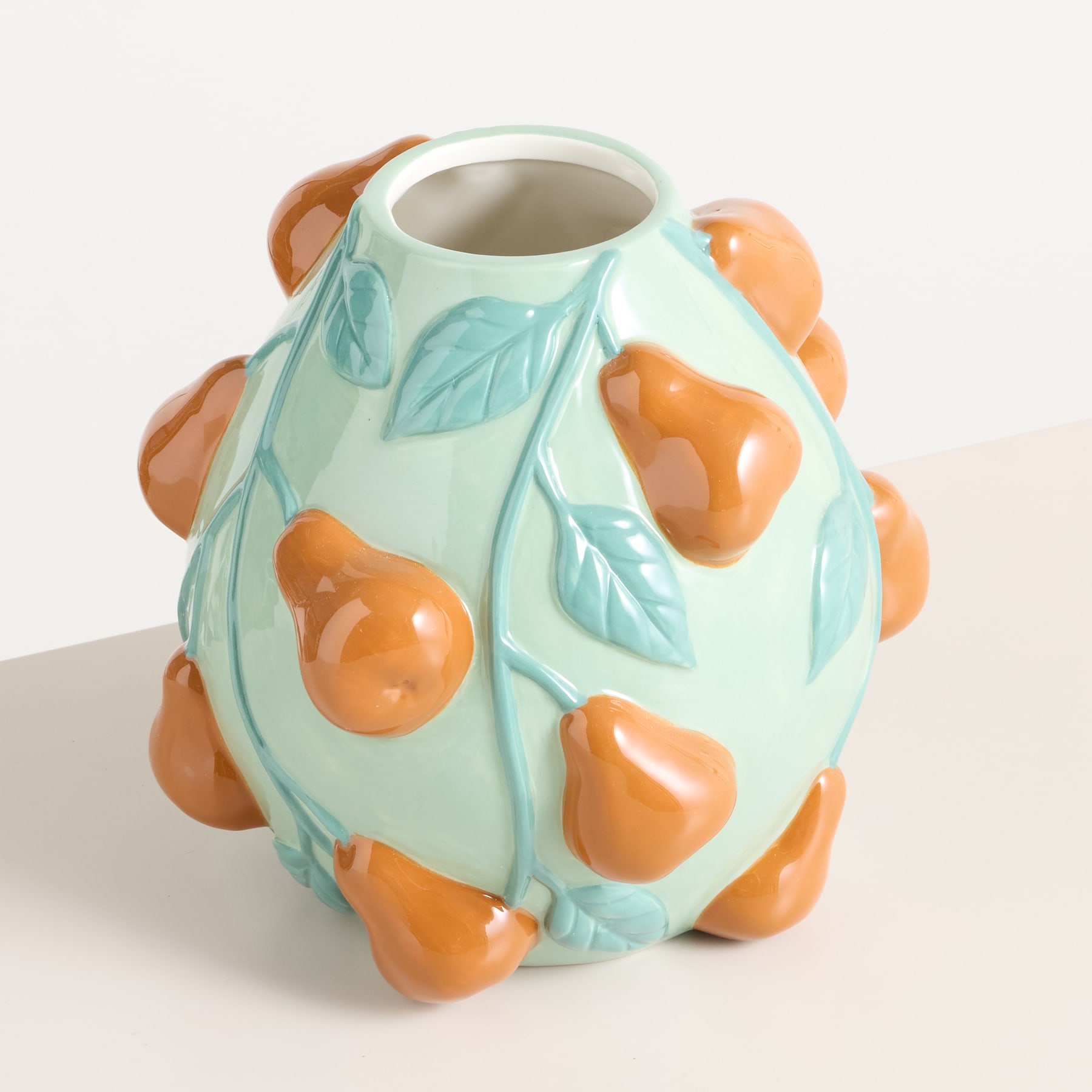 Eine Keramikvase mit mintgrüner Glasur und orangefarbenen birnenförmigen Mustern vor einem schlichten weißen Hintergrund.