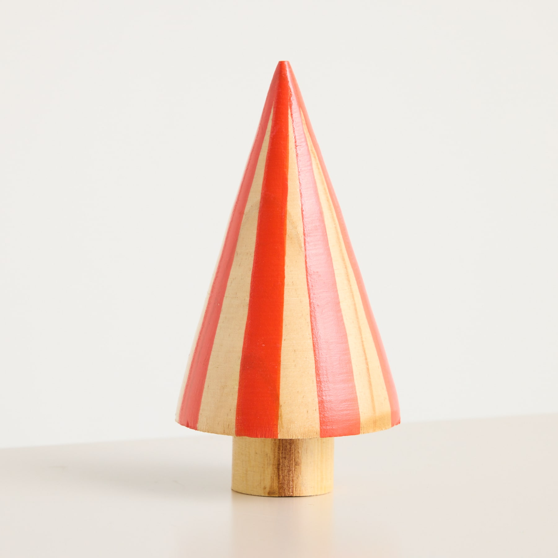 Ein farbenfrohes, kegelförmiges Holzobjekt mit abwechselnden Streifen in Orange- und Rosatönen steht vor einem schlichten, hellen Hintergrund.