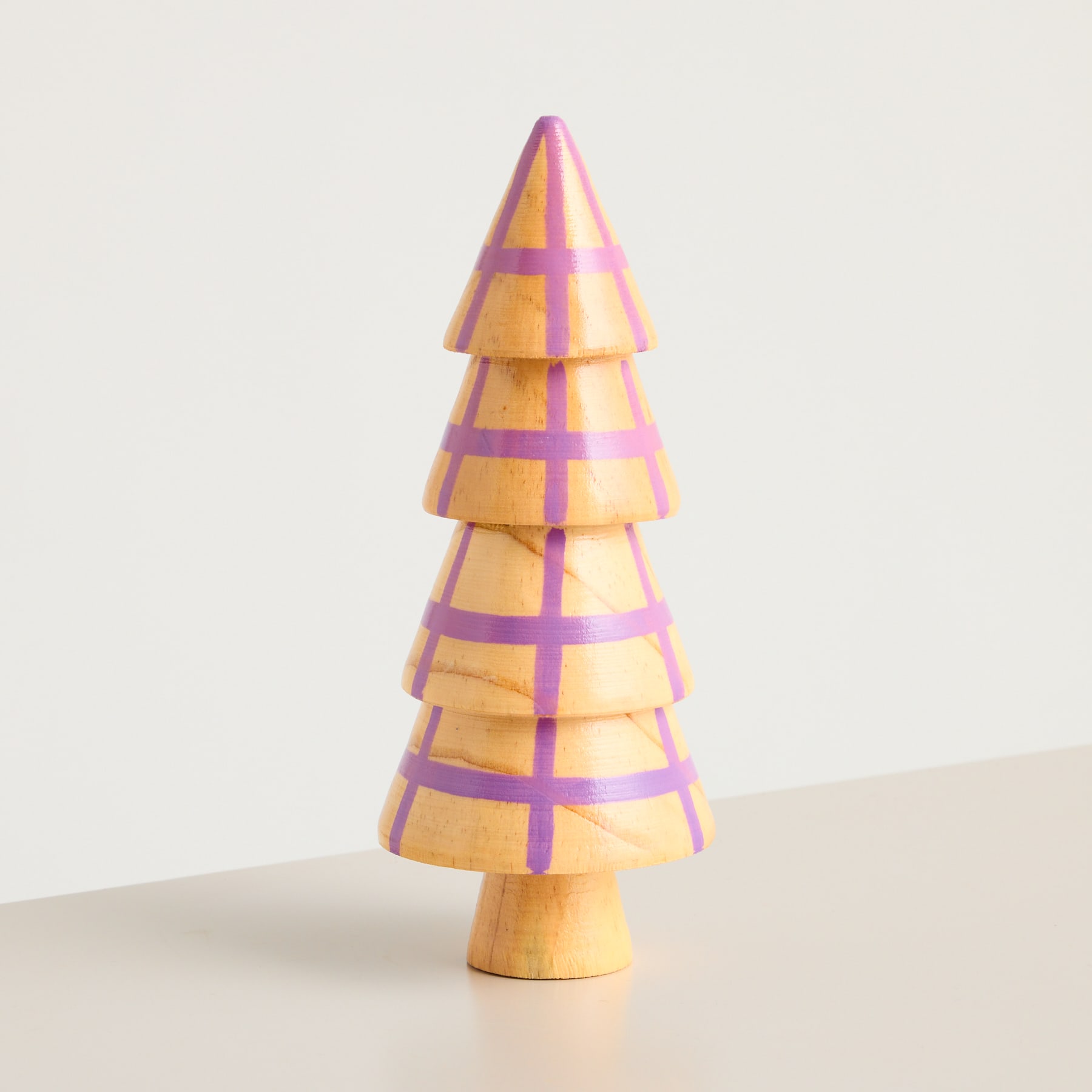 Auf einem schlichten weißen Hintergrund steht ein hölzernes, mehrschichtiges baumförmiges Objekt mit abwechselnd gelben und violetten Streifen.