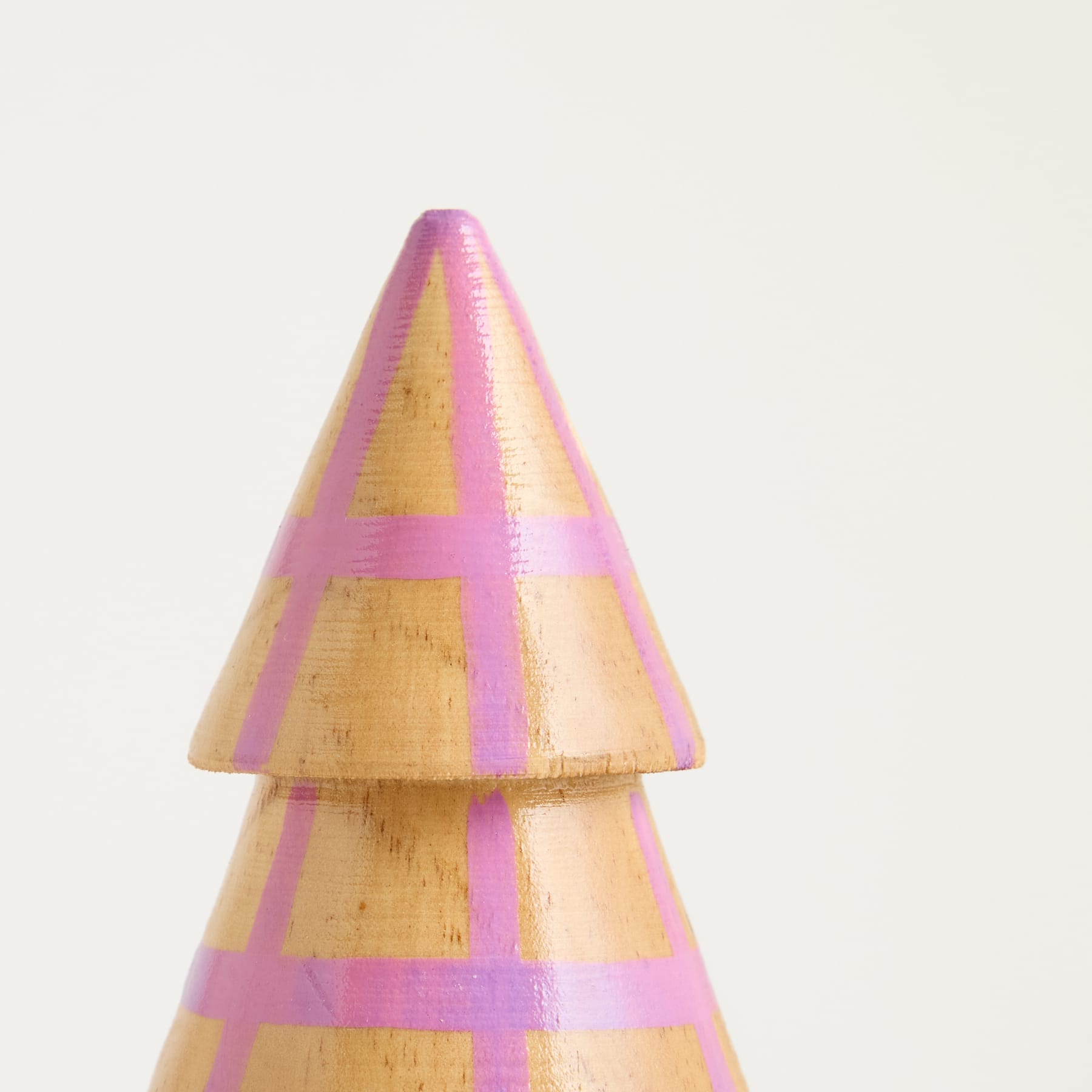 Vor einem schlichten weißen Hintergrund steht ein dreieckiges Holzobjekt mit rosa und gelben geometrischen Mustern.