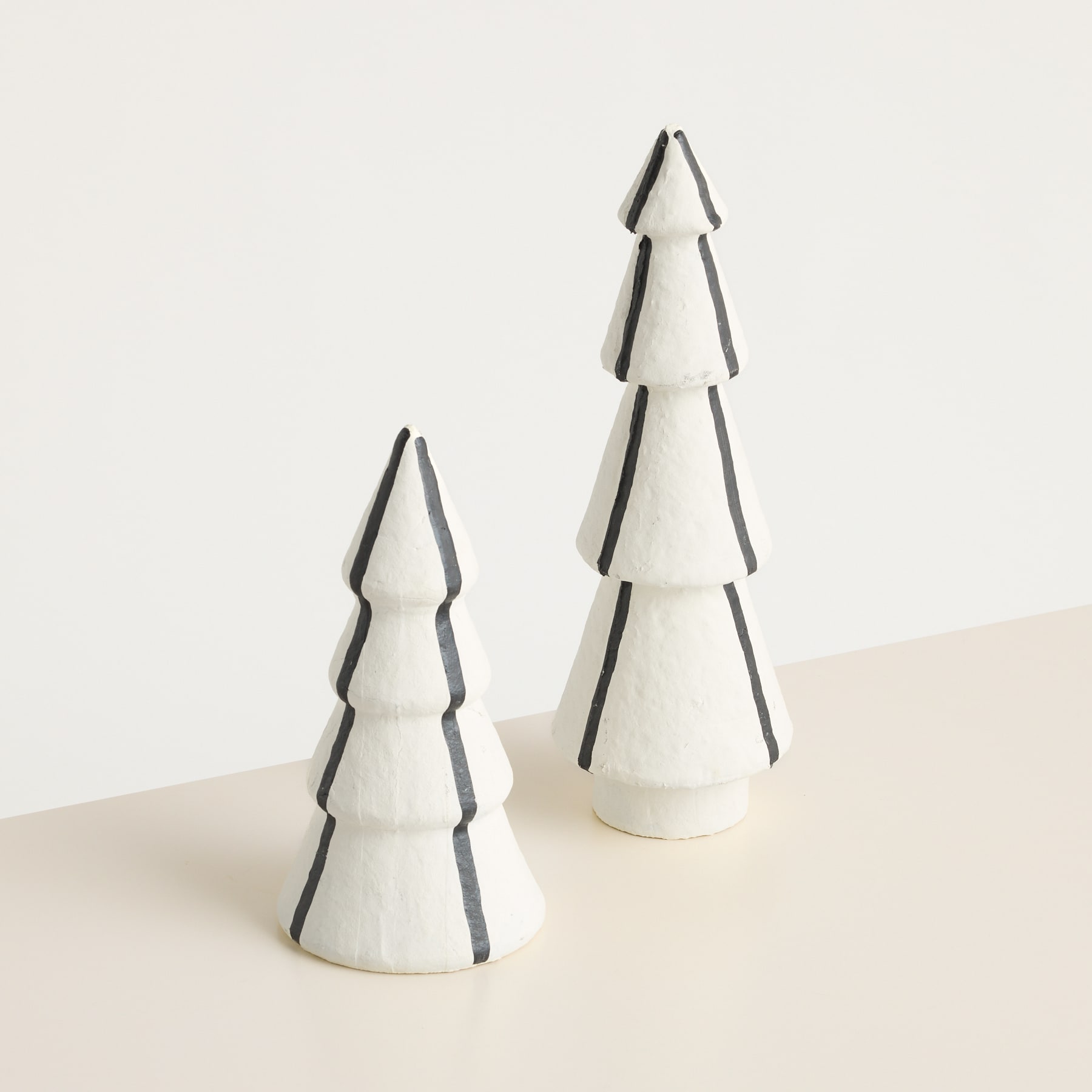 Zwei minimalistische weiße Keramik-Weihnachtsbäume mit schwarzen Akzenten stehen auf einer hellen Oberfläche vor einem schlichten Hintergrund.