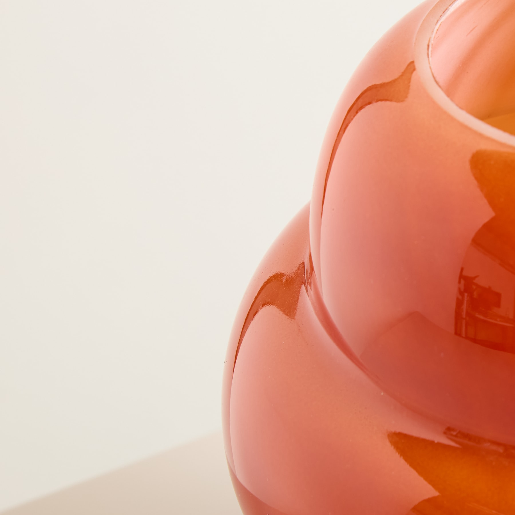 Ein leuchtend orangefarbenes Glasobjekt nimmt den Großteil des Rahmens ein, während ein schlichter, heller Hintergrund einen einfachen und minimalistischen Hintergrund bietet.