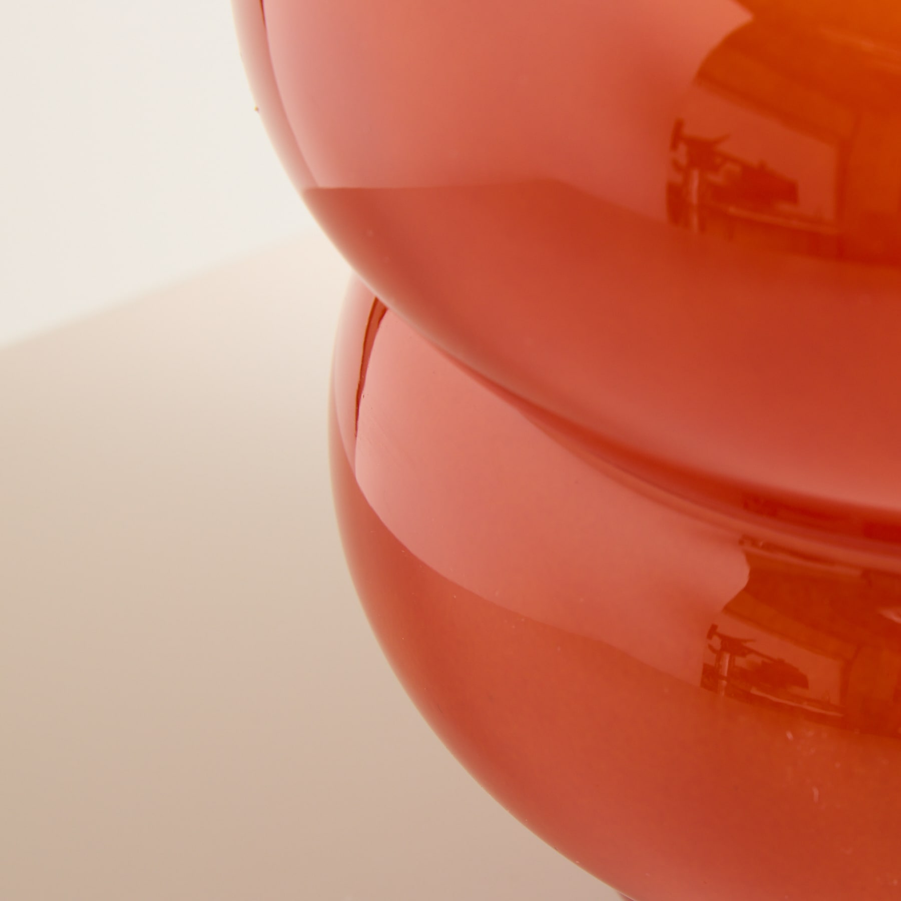 Ein leuchtendes, rot-oranges Glasobjekt füllt den Rahmen vor einem unscharfen, hellen Hintergrund.
