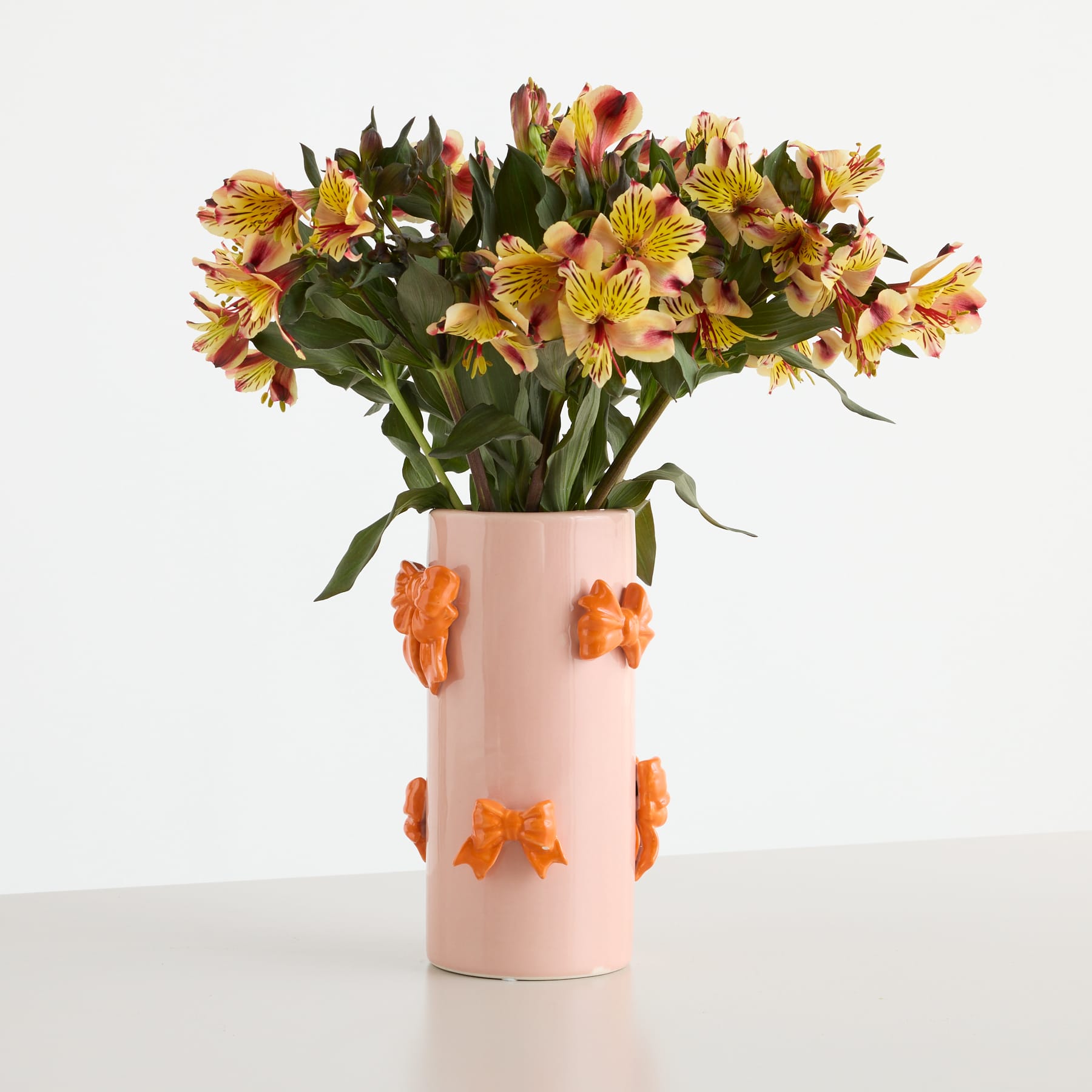 Auf einem schlichten weißen Hintergrund steht eine Vase mit einem farbenfrohen Strauß gelber und orangefarbener Inkalilien.
