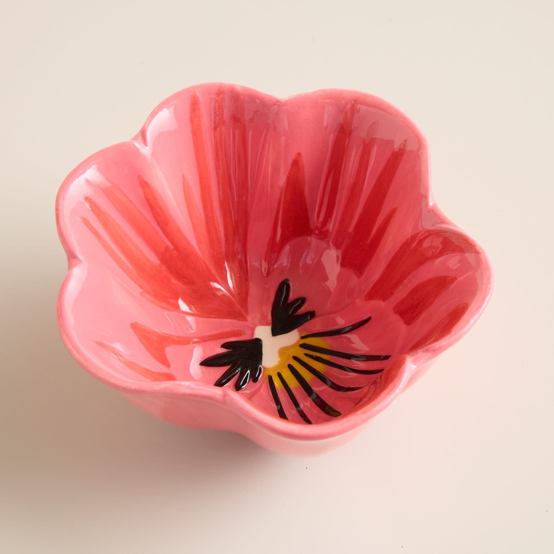 Eine lebendige Nahaufnahme einer rosa Stiefmütterchenblüte mit zarten Blütenblättern und einer auffälligen schwarz-gelben Mitte vor einem neutralen beigen Hintergrund.