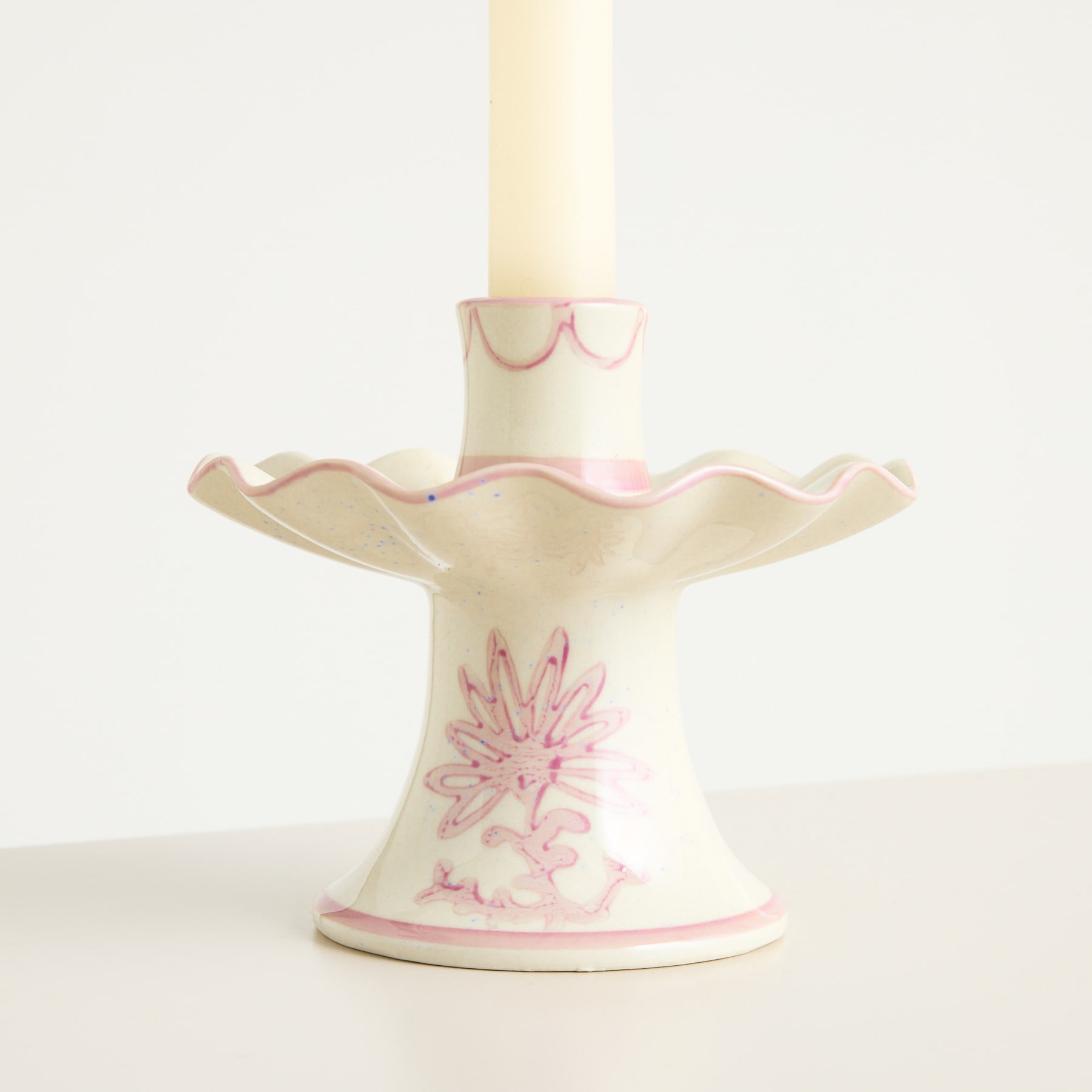 Ein dekorativer Kerzenhalter aus Keramik mit Blumenmuster und gewelltem, gezacktem Rand steht auf einer hellen Oberfläche vor einem schlichten Hintergrund.