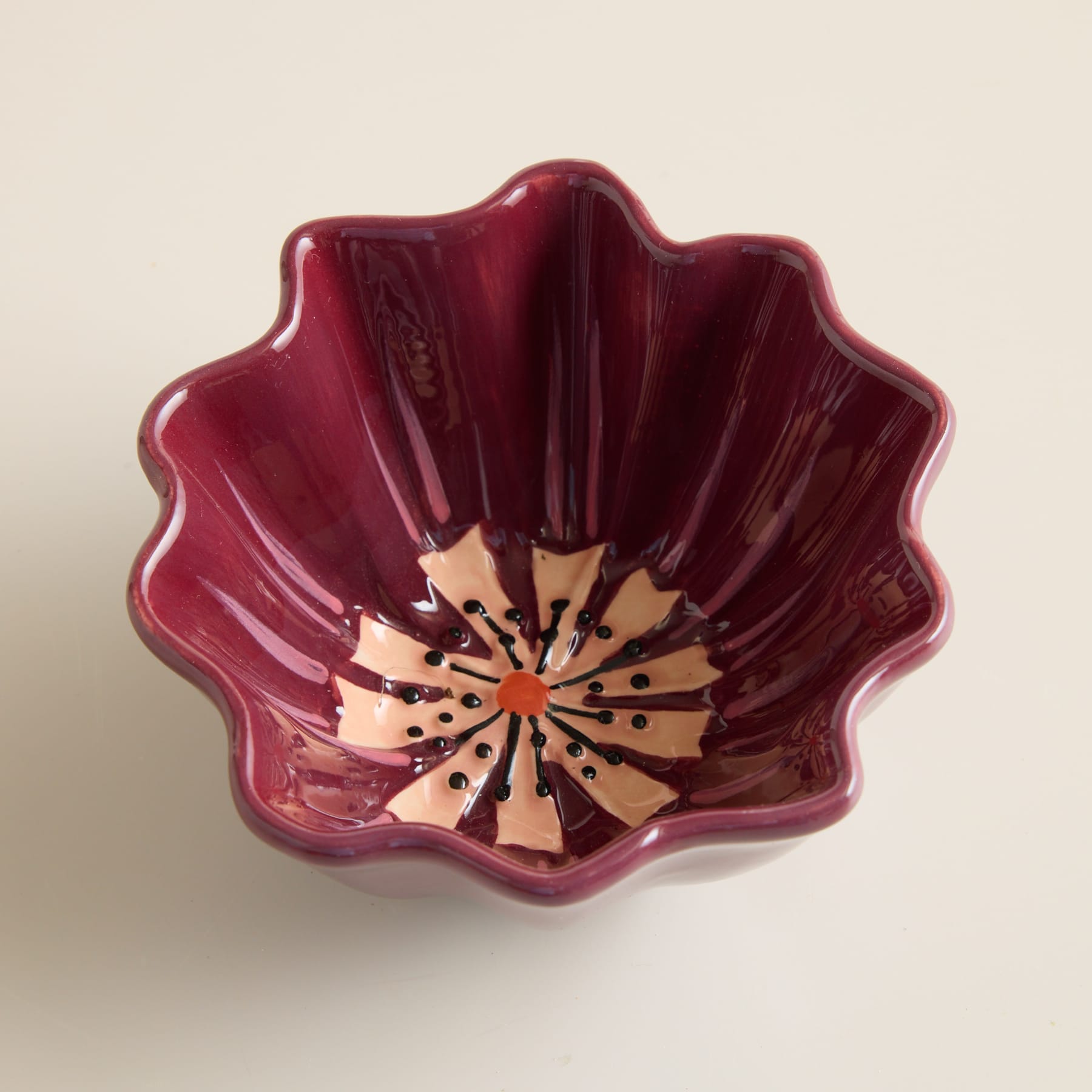 Eine leuchtend tiefrote Keramikschale mit Blumenmuster vor einem neutralen Hintergrund.