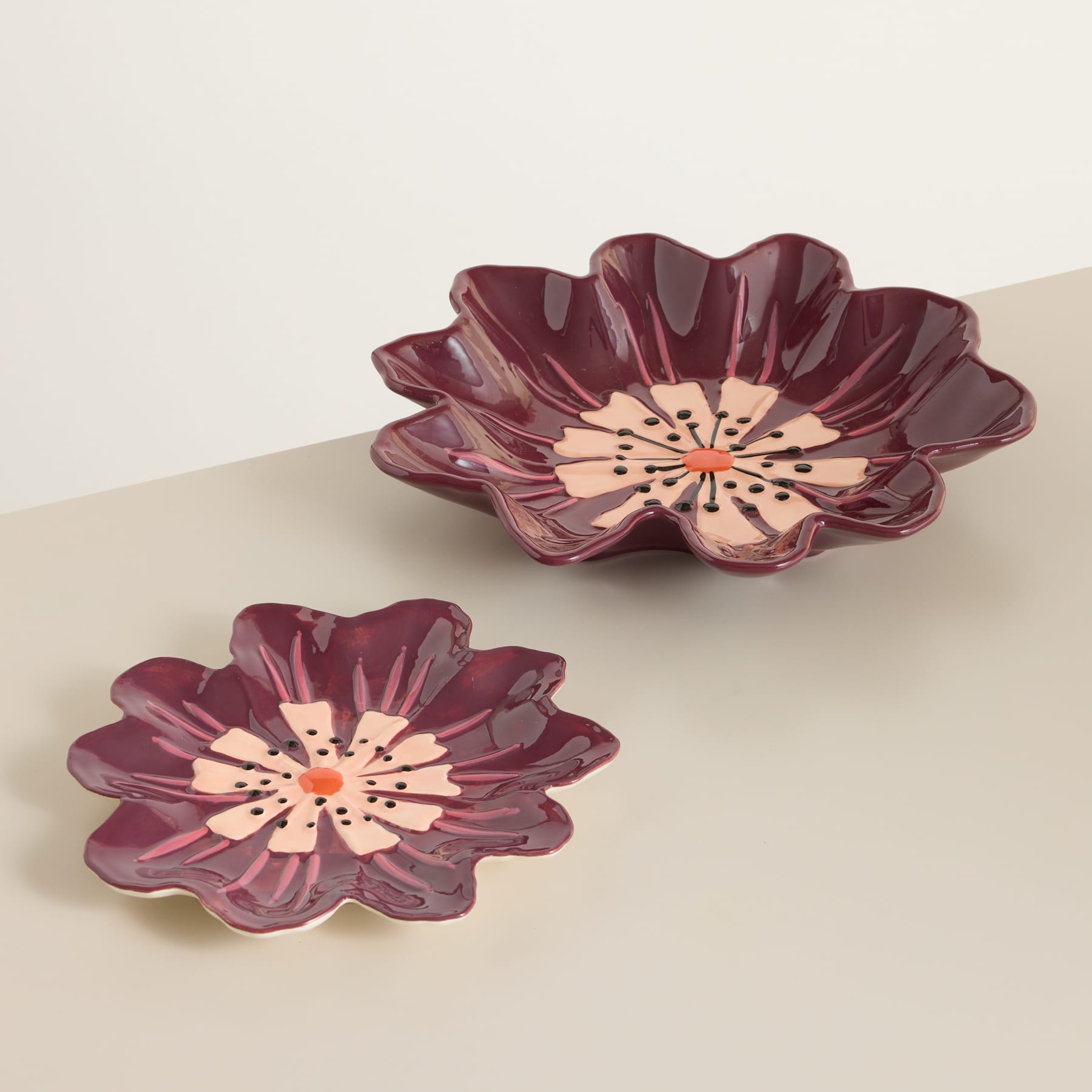 Zwei burgunderfarbene Keramikschalen oder -teller in Blumenform werden auf einer hellen Oberfläche mit schlichtem Hintergrund präsentiert.