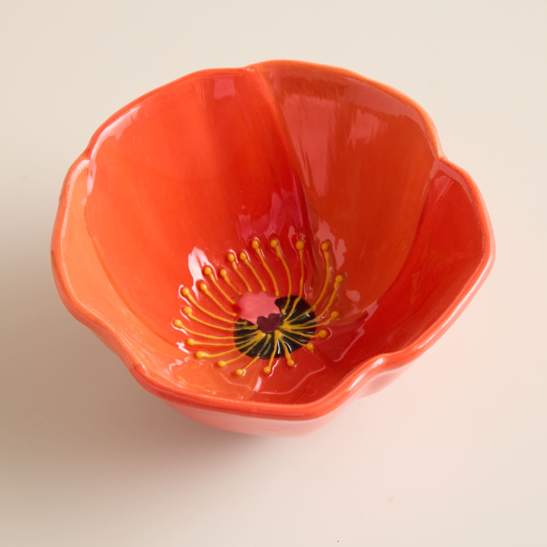 Eine leuchtend rote Mohnblüte mit ihren zarten Blütenblättern und der kunstvollen Mitte ist der Mittelpunkt des Bildes, vor einem schlichten, hellen Hintergrund.