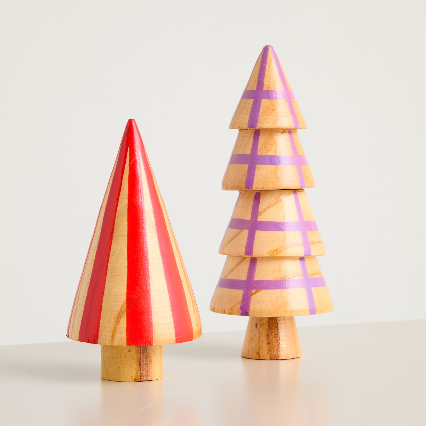 Zwei bunte Weihnachtsbäume aus Holz in verschiedenen Formen und Größen stehen auf einem schlichten Hintergrund.