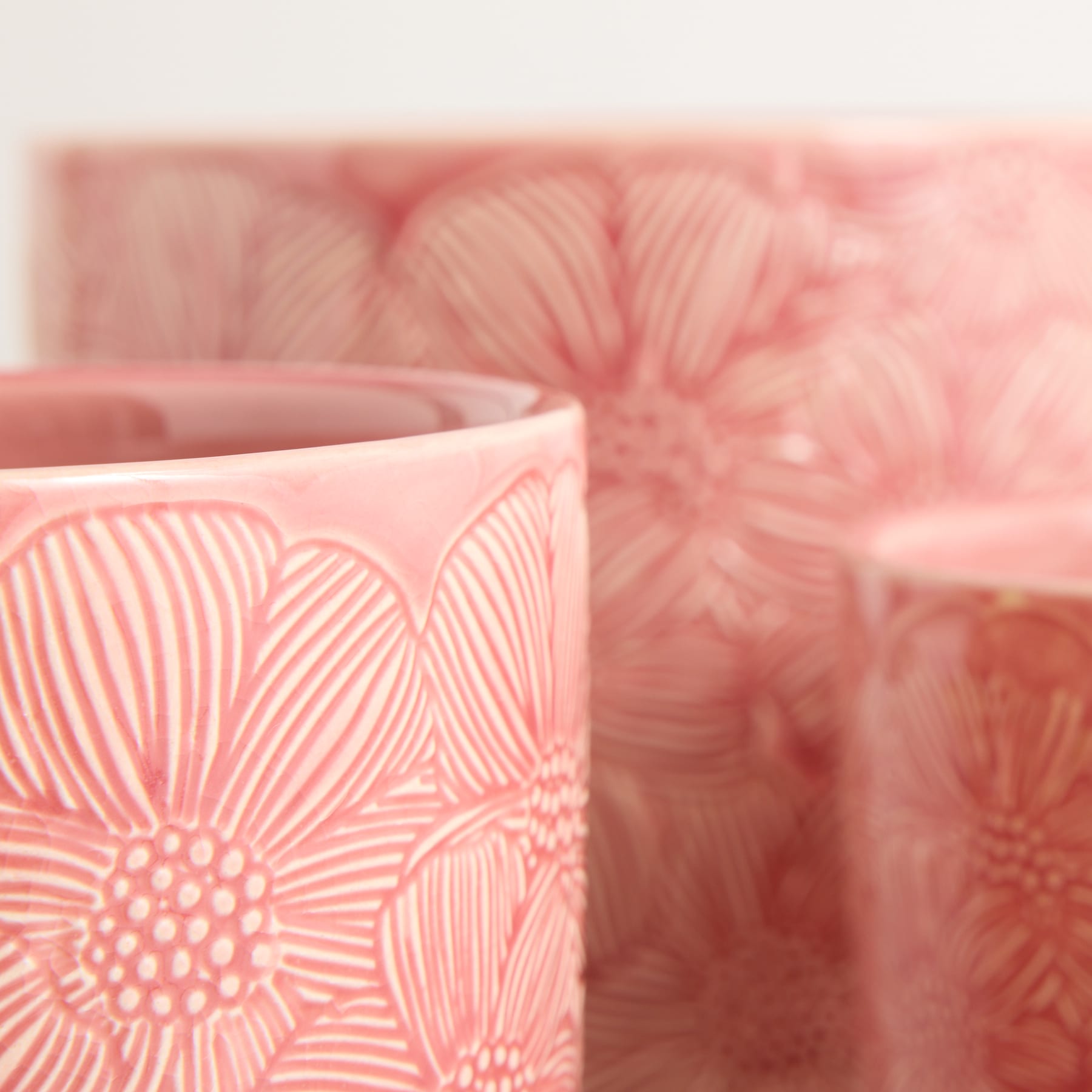 Im Vordergrund steht eine rosa Keramiktasse mit Blumenmuster, während ein verschwommener, zartrosa Hintergrund eine verträumte, ätherische Atmosphäre schafft.