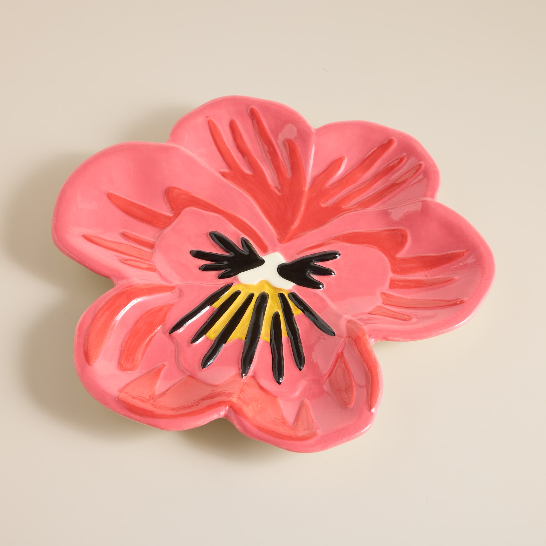 Eine leuchtend rosa Blume mit zarten Blütenblättern und einer kräftigen schwarzen Mitte hebt sich von einem neutralen, beigen Hintergrund ab.