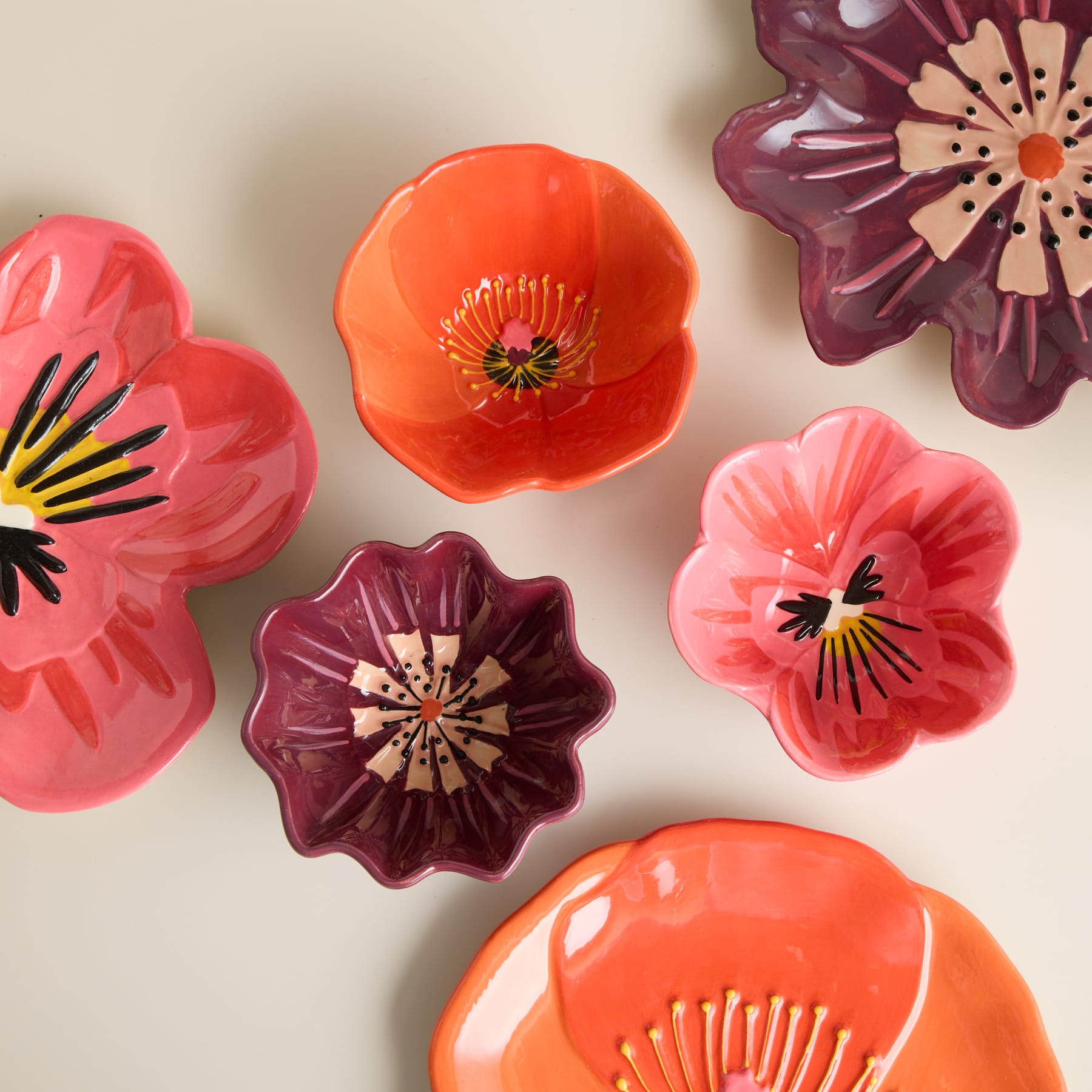 Lebendige, farbenfrohe Keramikblumen in Orange-, Rosa- und Lilatönen zieren einen neutral getönten Hintergrund.