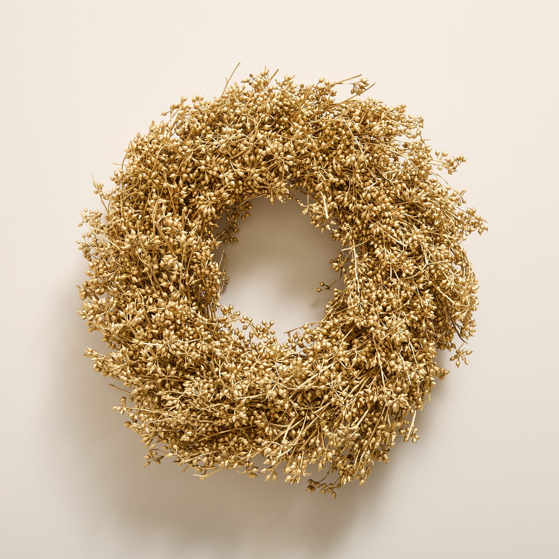 Vor einem schlichten, hellen Hintergrund wird ein goldener Kranz aus getrockneten Blumen oder Zweigen präsentiert.