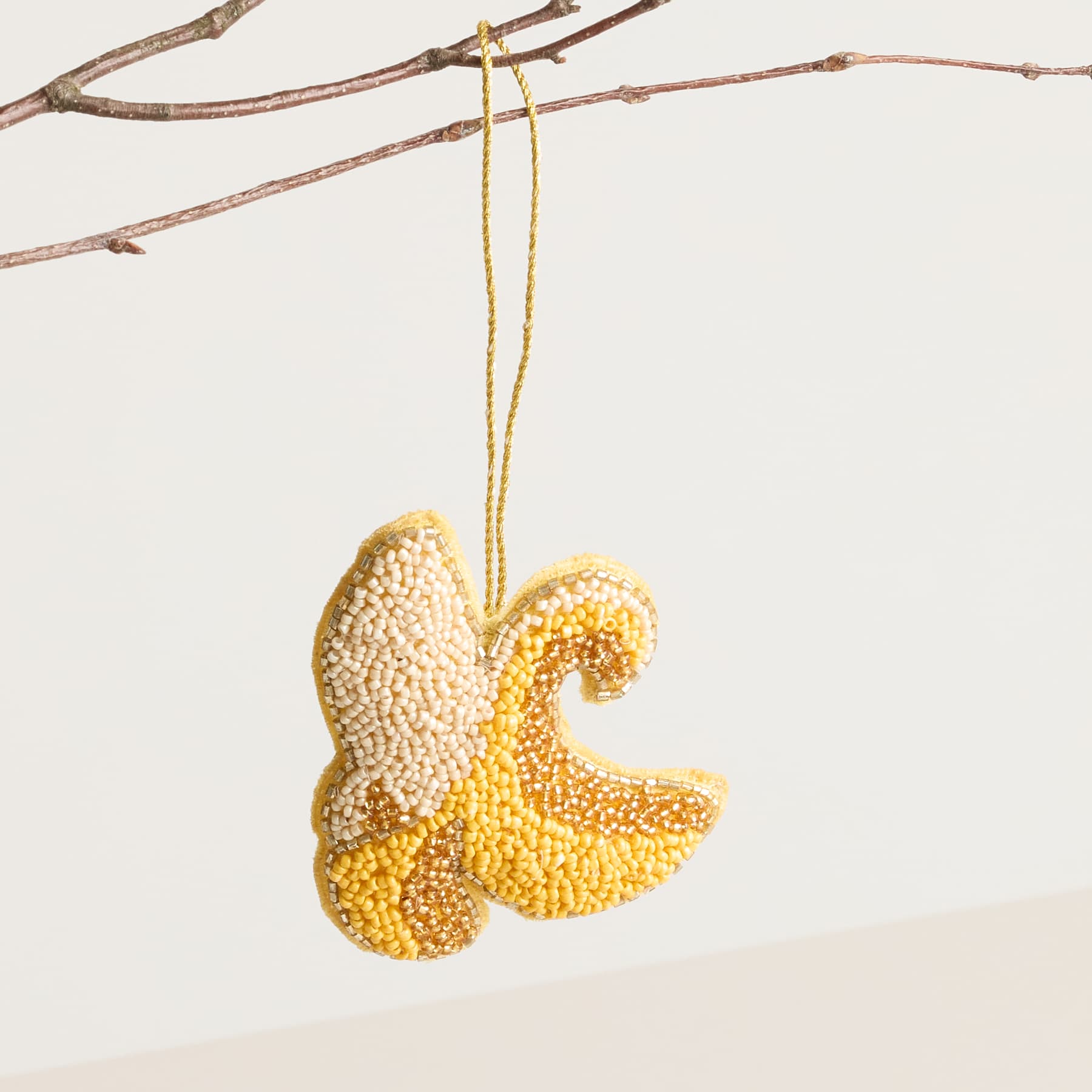 Ein goldenes, strukturiertes Ornament in Form eines Schmetterlings oder einer Motte hängt vor einem schlichten weißen Hintergrund an einem Ast.