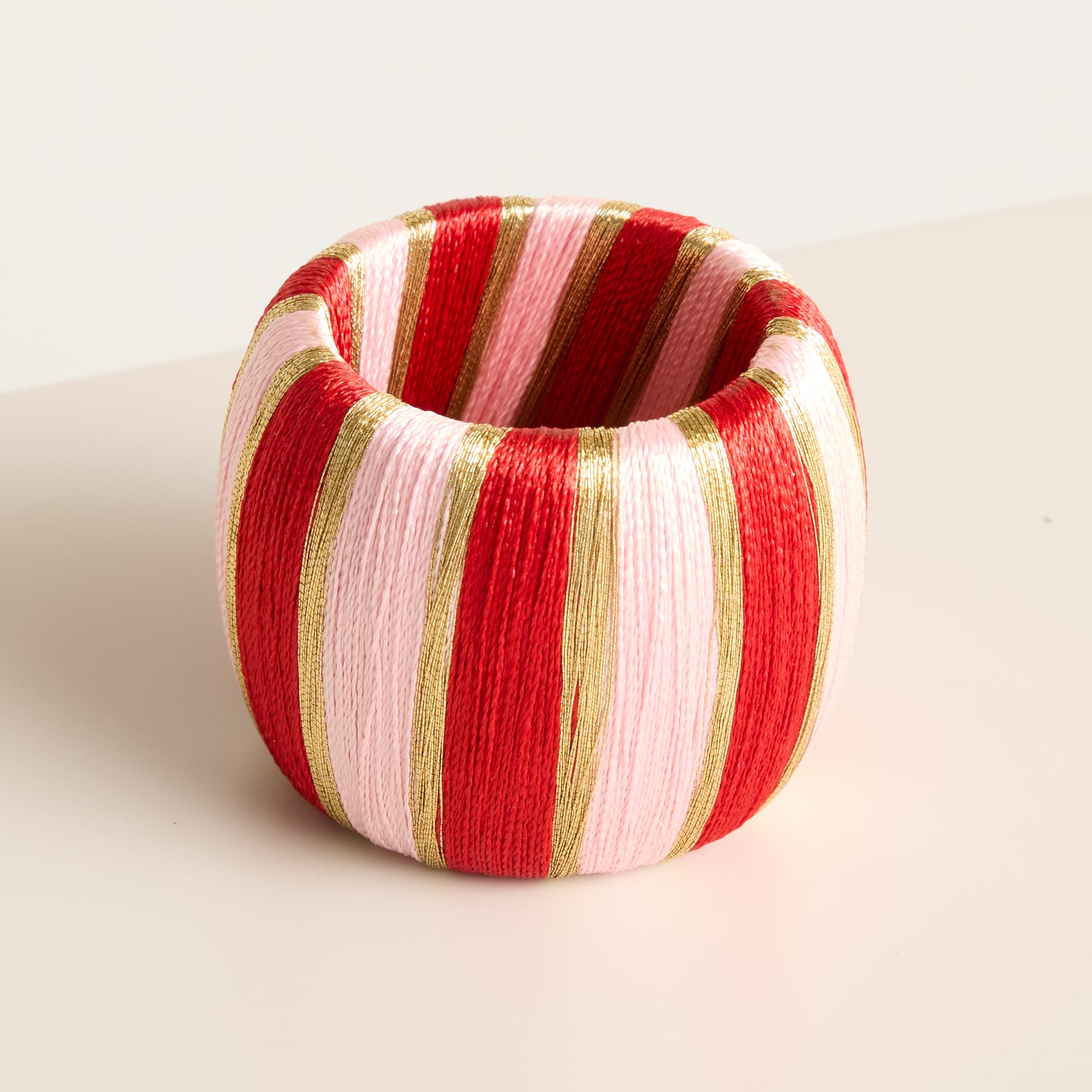 Auf einer hellen Oberfläche steht ein bunt gestreiftes, schalenförmiges Objekt aus gewebtem Material.