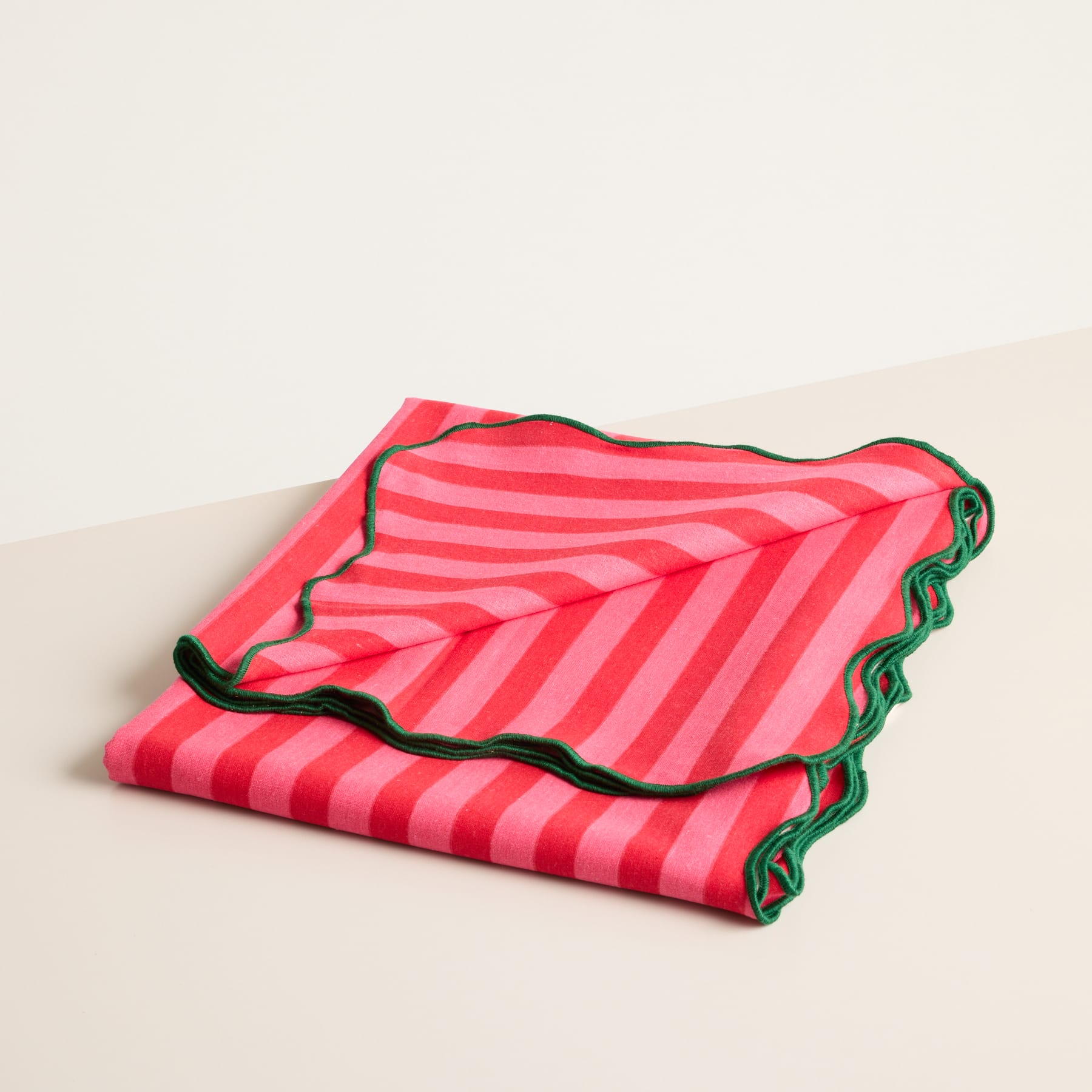 Auf einer hellen Oberfläche liegt ein leuchtend rot-rosa gestreifter Stoff mit gewelltem, gezacktem Rand.