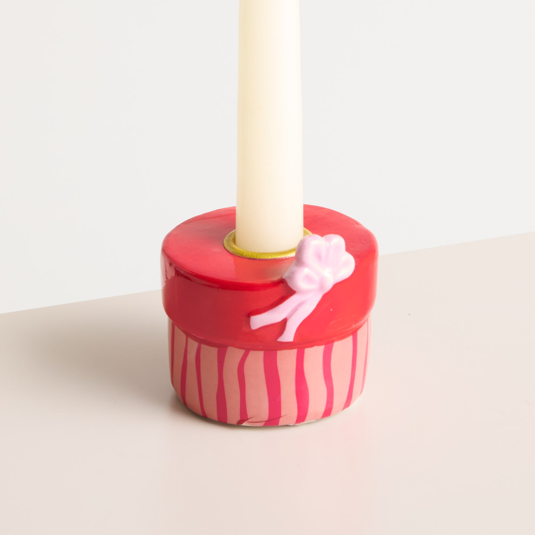 Auf einer hellen Fläche steht ein rotes zylindrisches Objekt mit einer rosafarbenen, blumenförmigen Verzierung, aus dessen Mitte eine weiße Kerze ragt.