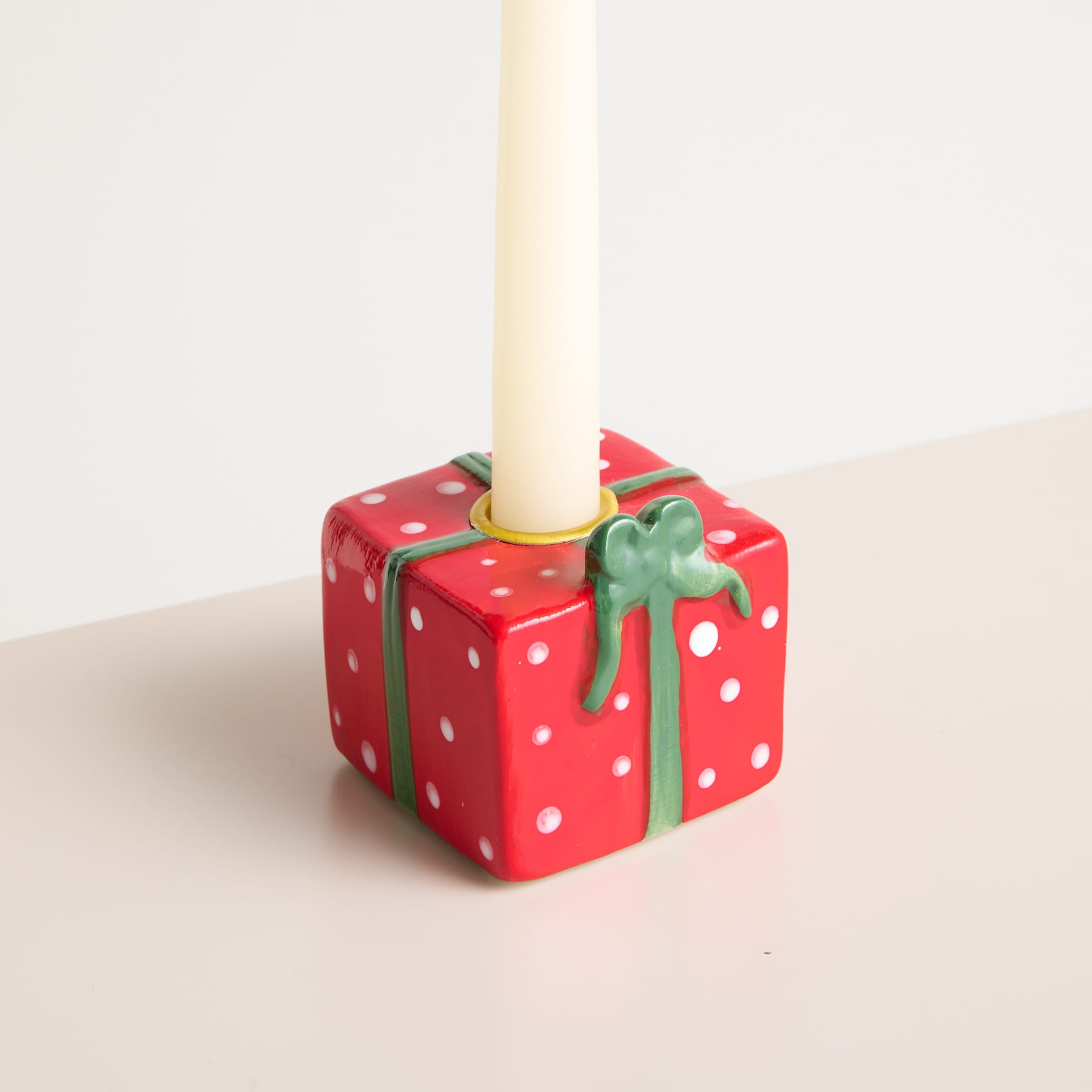 Auf einer hellen Fläche steht eine rot gepunktete Geschenkbox mit grüner Schleife, aus deren Oberseite eine weiße Kerze herausragt.