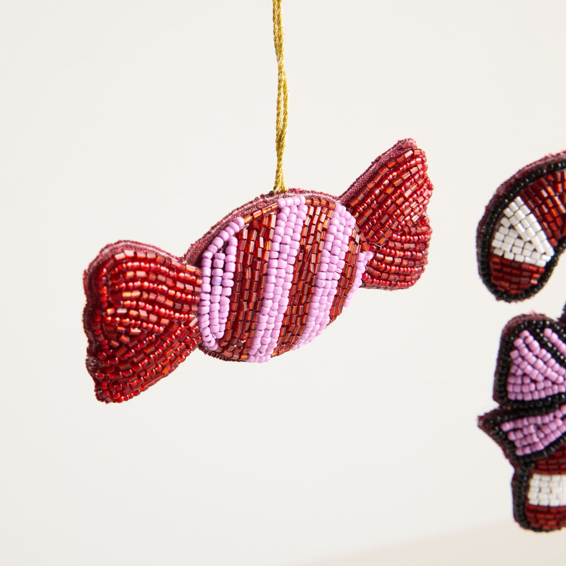 Ein farbenfrohes, perlenbesetztes Ornament in Bonbonform hängt vor einem schlichten, hellen Hintergrund.