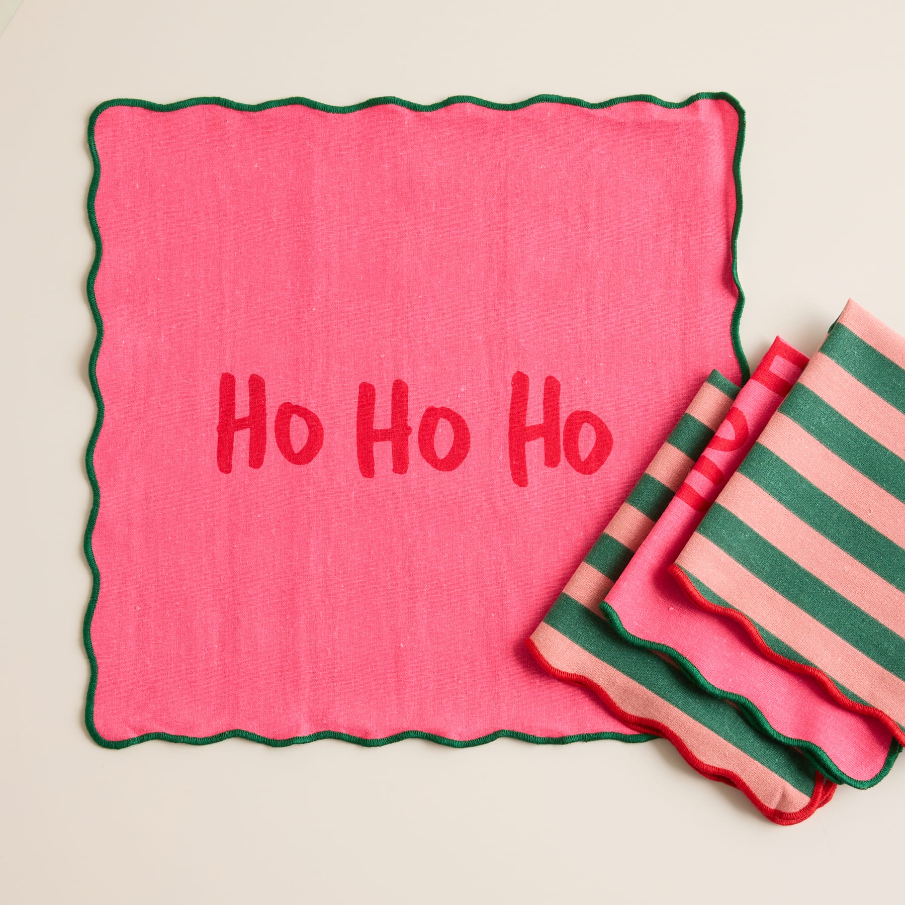 Ein leuchtend rosa Papier mit dem Text „Ho Ho Ho“, umgeben von bunt gestreiftem Geschenkpapier im Hintergrund.