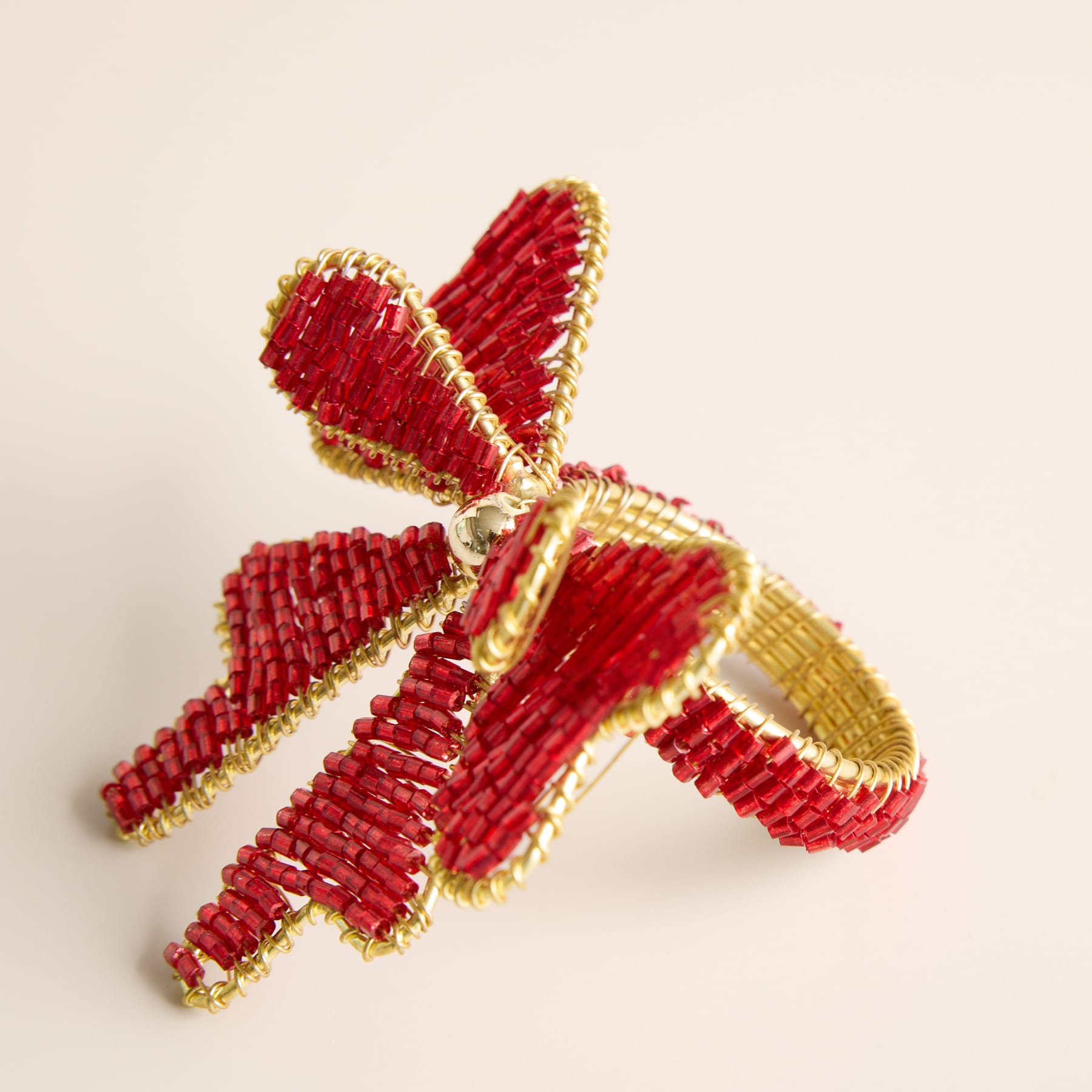Ein leuchtendes, kompliziertes Ornament oder eine Dekoration aus roten und goldenen Perlen in Schmetterlings- oder Libellenform auf einem schlichten, hellen Hintergrund.