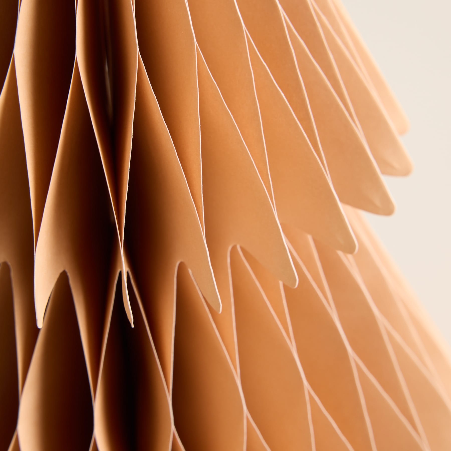 Schichten aus warm getönten, überlappenden Papier- oder Stoffformen erzeugen im Vordergrund vor einem neutralen Hintergrund ein optisch auffälliges und strukturiertes Muster.