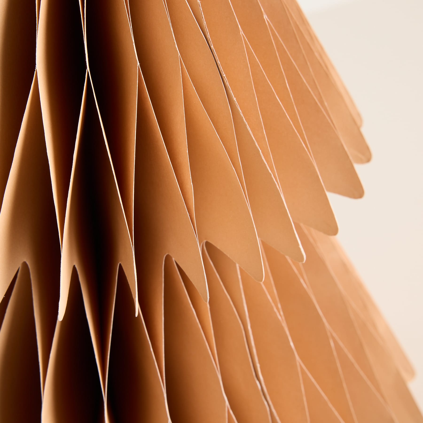 Schichten aus warmem, überlappendem Papier oder Karton bilden vor einem neutralen Hintergrund ein strukturiertes, fächerartiges Muster.