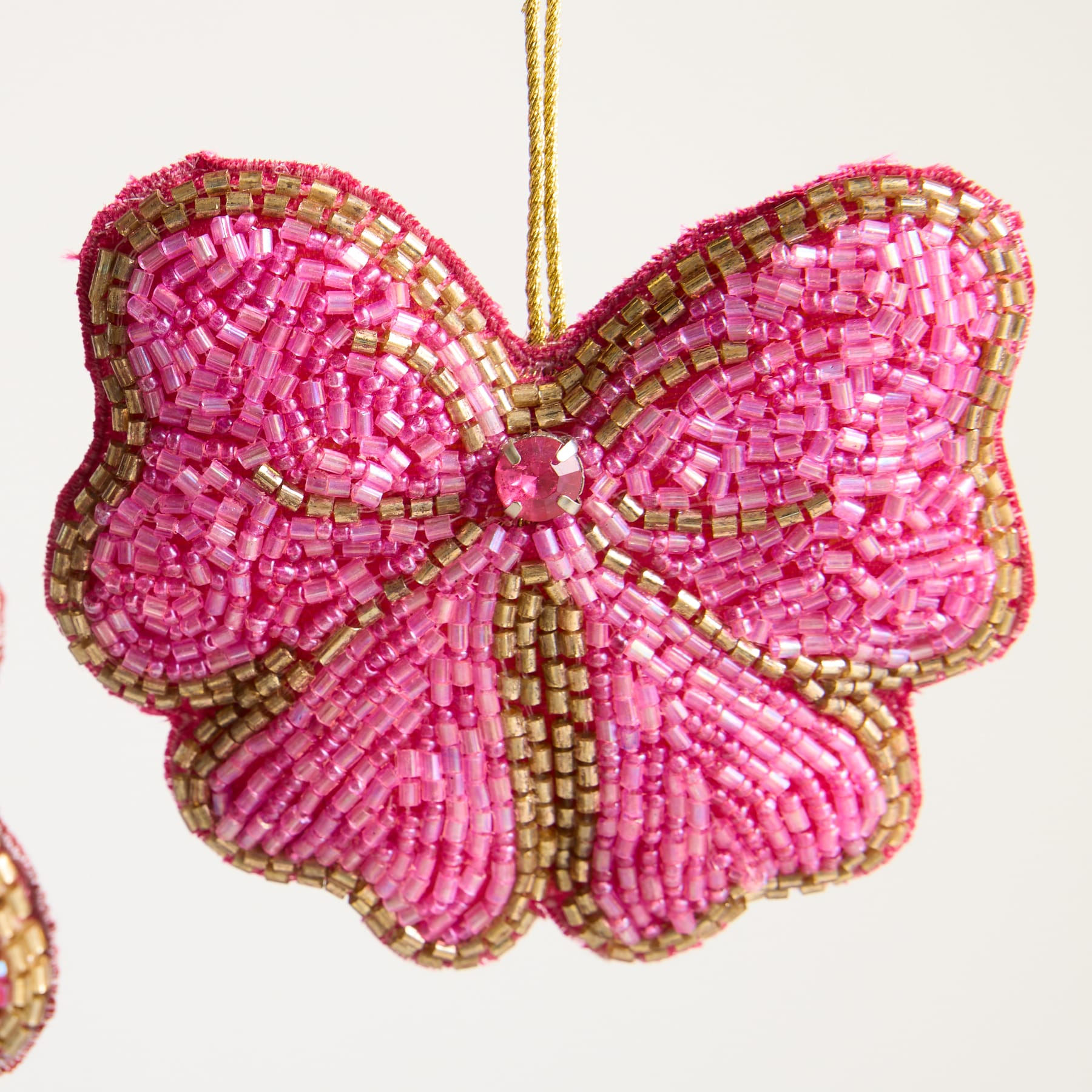 Ein leuchtendes Schmetterlingsornament aus Perlen mit komplizierten rosa und goldenen Mustern auf einem schlichten, hellen Hintergrund.