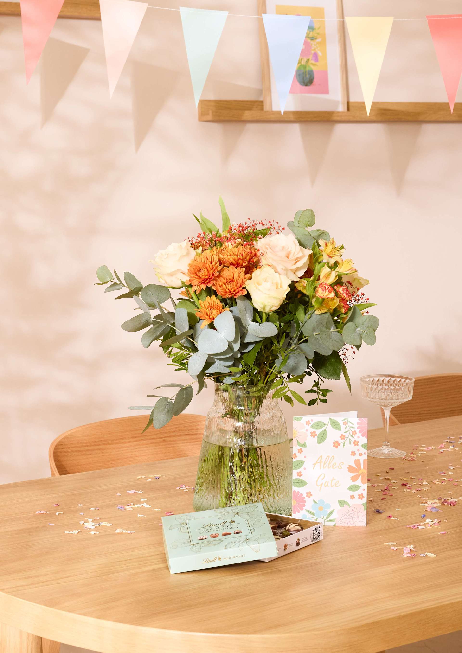 Ein bunter Blumenstrauß steht auf einem Holztisch, umgeben von festlicher Dekoration und Backwaren, und sorgt für eine fröhliche und festliche Atmosphäre.