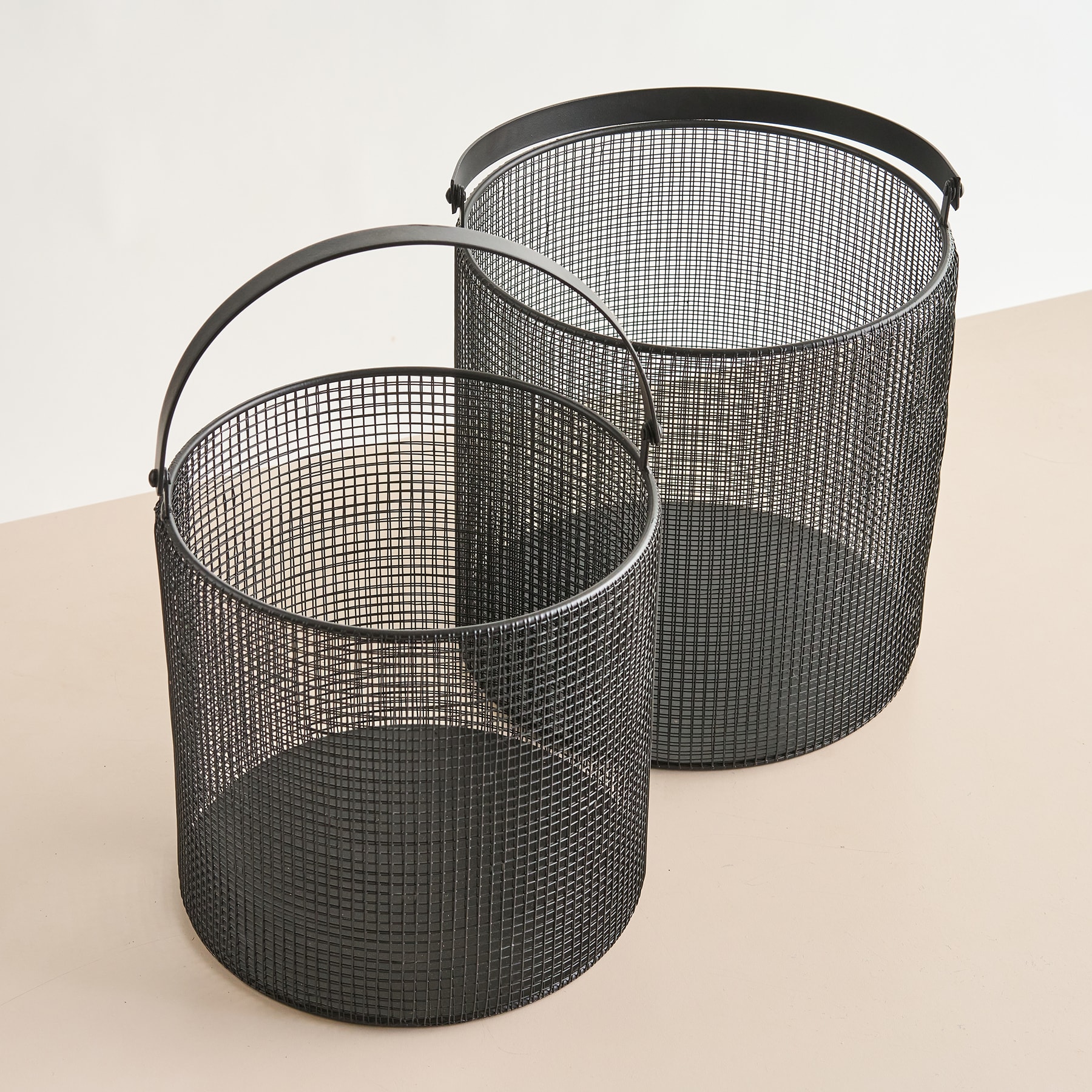 Zwei zylindrische Drahtgeflechtkörbe unterschiedlicher Größe stehen auf einer hellen Oberfläche und bilden eine minimalistische und industriell inspirierte Komposition.