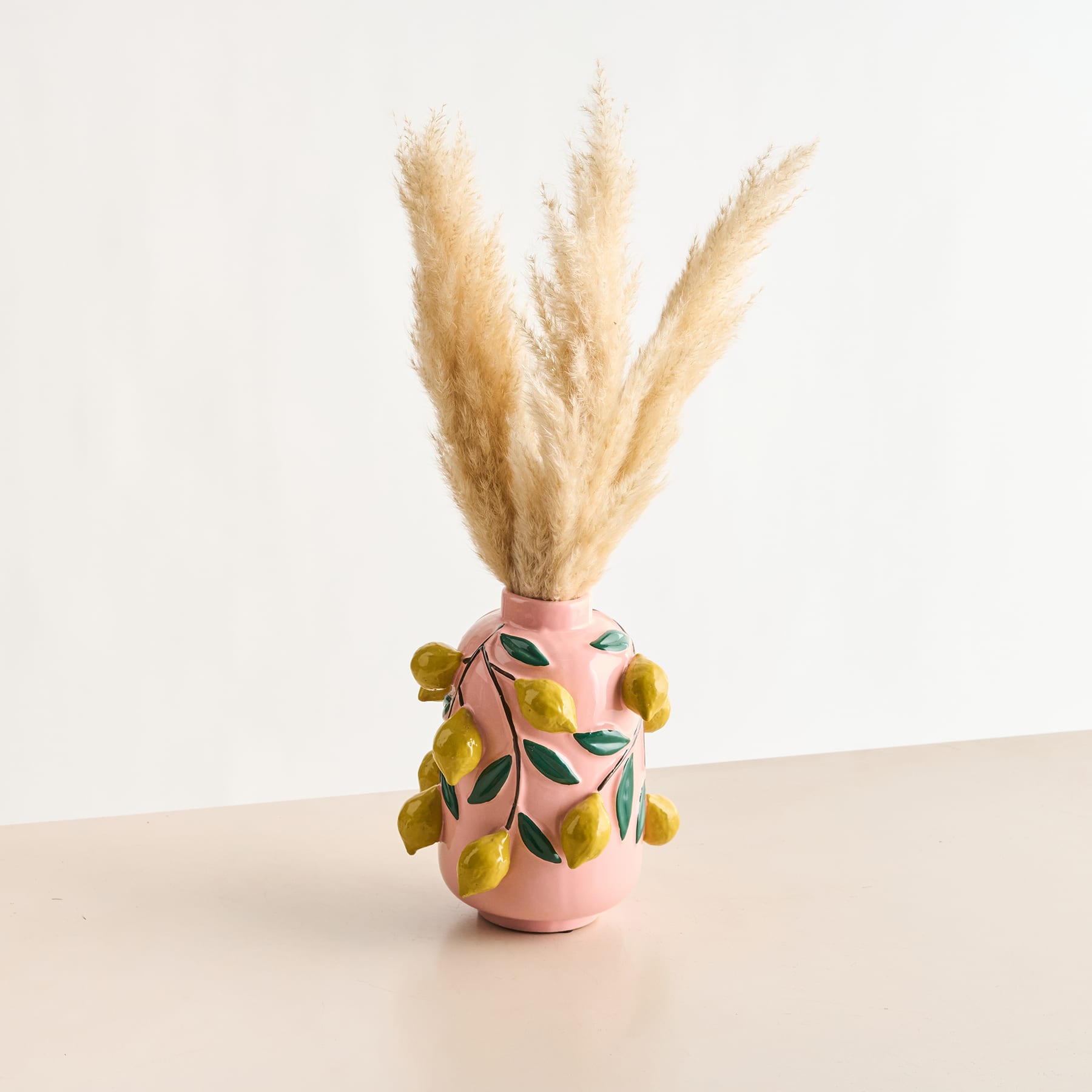 Eine rosafarbene Keramikvase mit einem Muster aus leuchtend gelben Zitronen und grünen Blättern, die ihre Oberfläche schmücken.