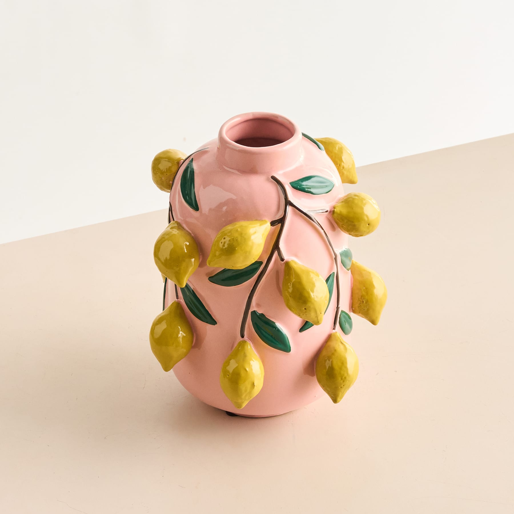Eine rosa Keramikvase mit Blumenmuster hält einen Strauß flauschigen, goldenen Pampasgrases vor einem schlichten, hellen Hintergrund.