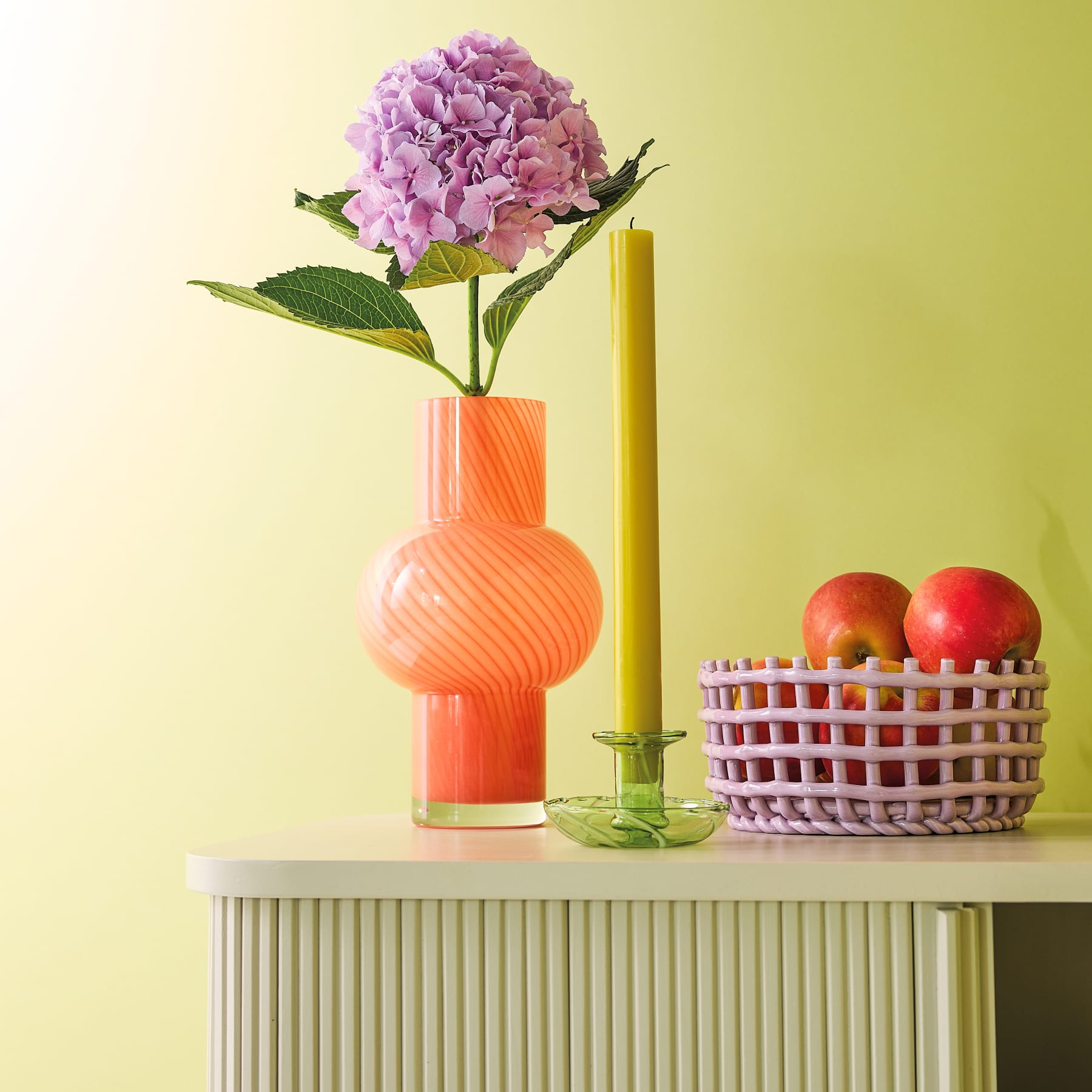 Zwei leuchtend violette Alliumblüten werden in einer einfachen, orangefarbenen Vase vor einem schlichten, hellen Hintergrund präsentiert.