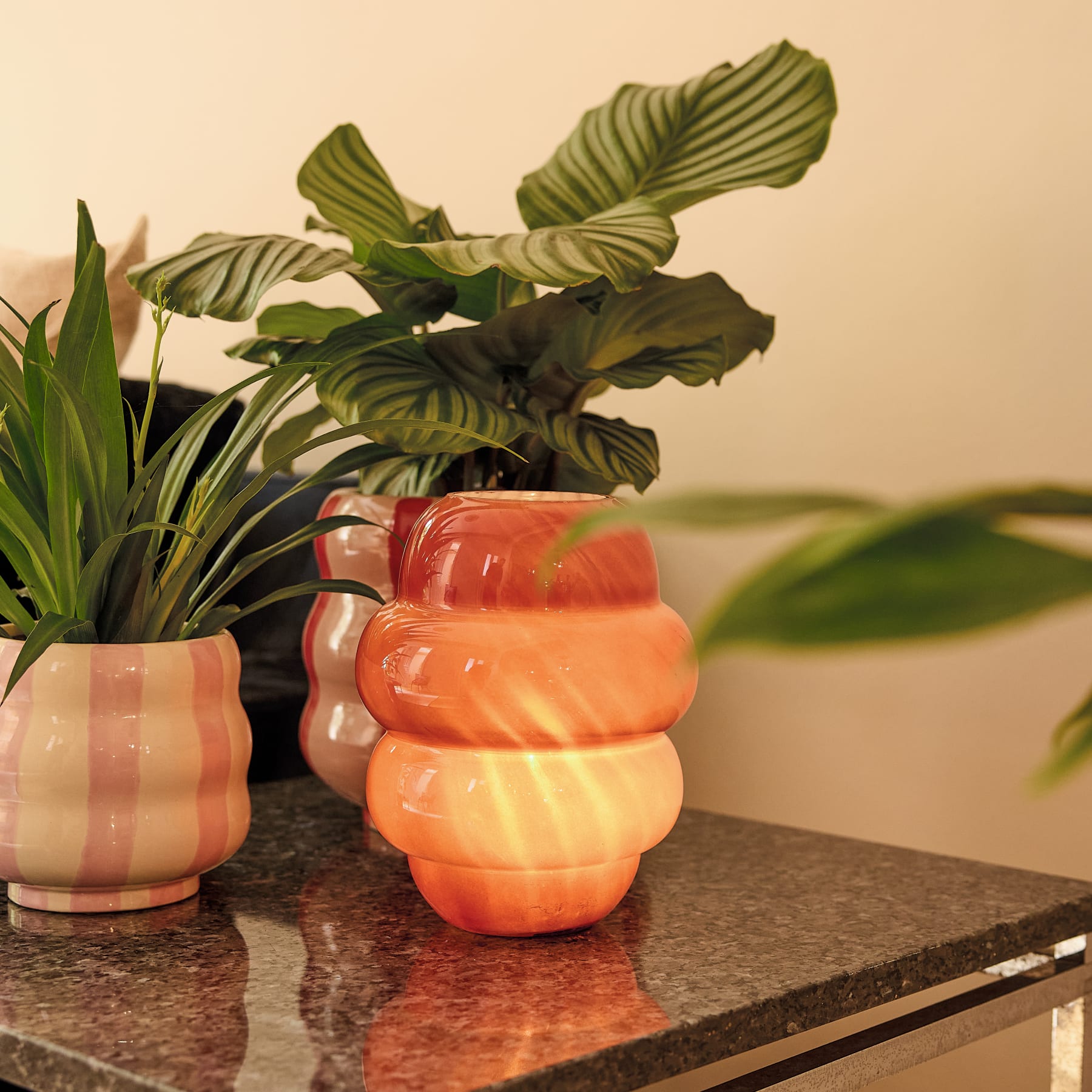 Eine leuchtend orangefarbene Keramikvase mit einem einzigartigen, gestapelten Design steht auf einer schlichten, hellen Oberfläche.