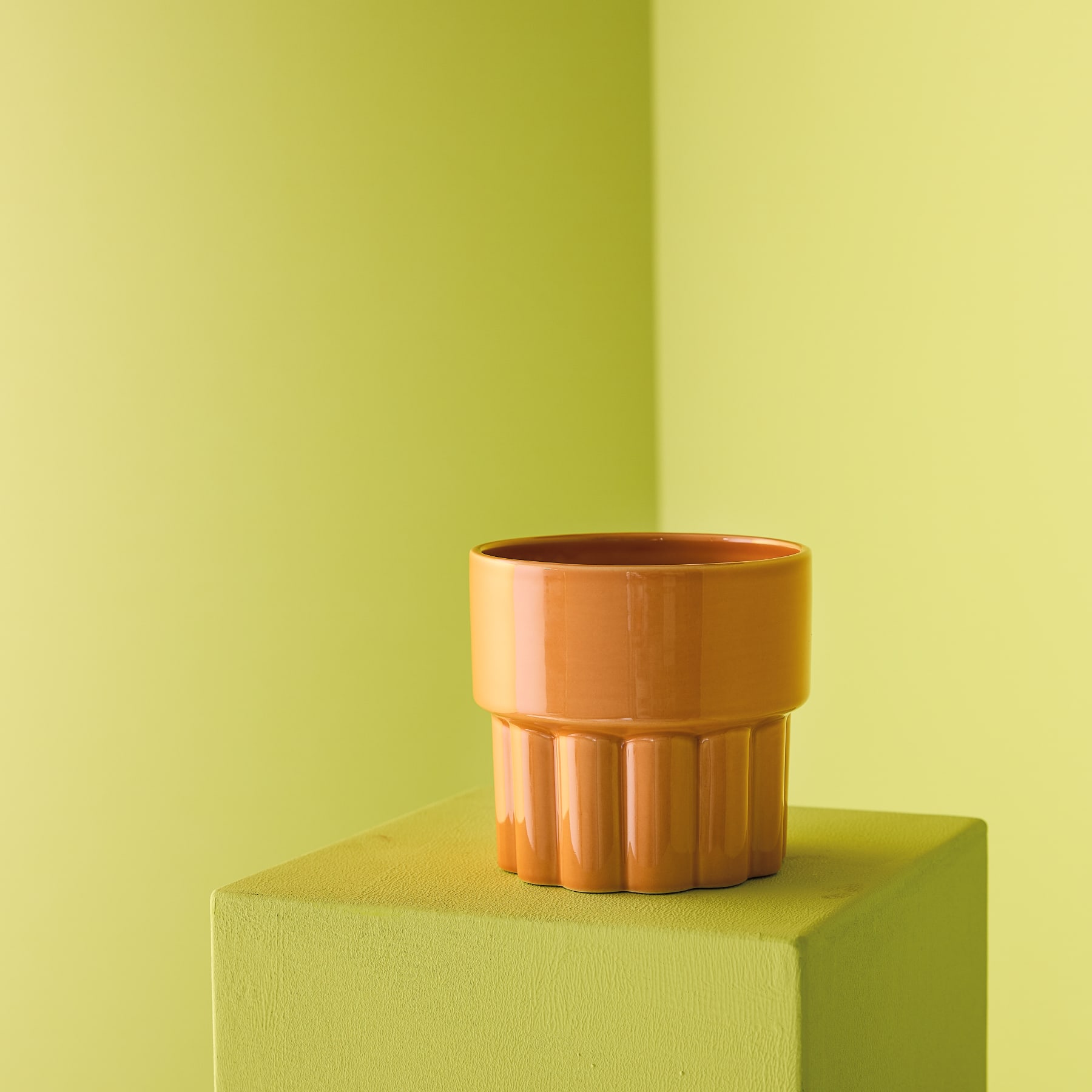 Ein leuchtend orangefarbener Blumentopf oder eine Vase aus Keramik mit strukturierter, gerippter Außenseite steht auf einer schlichten, hellen Oberfläche.